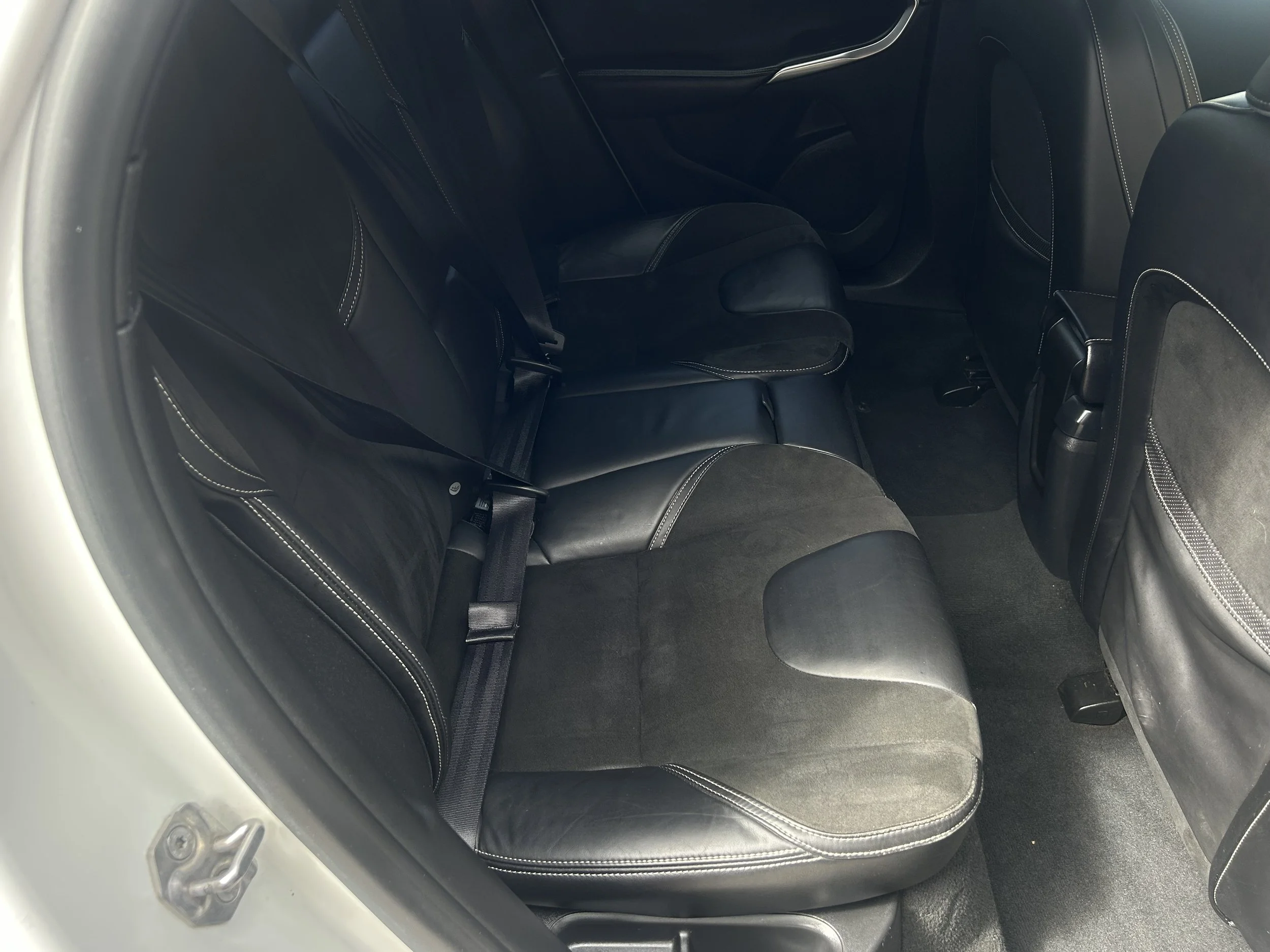 Rear interior of a car showing black leather and fabric seats, seat belts, and floor mats.