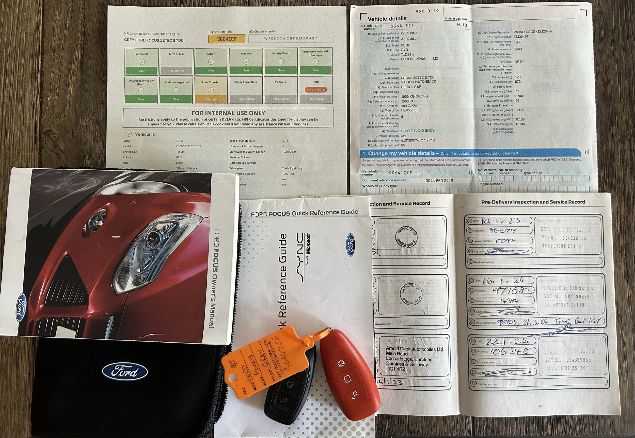 Car service records, vehicle documentation, car key fob, Ford owner's manual, and a Ford-branded zippered pouch laid out on a wooden surface.