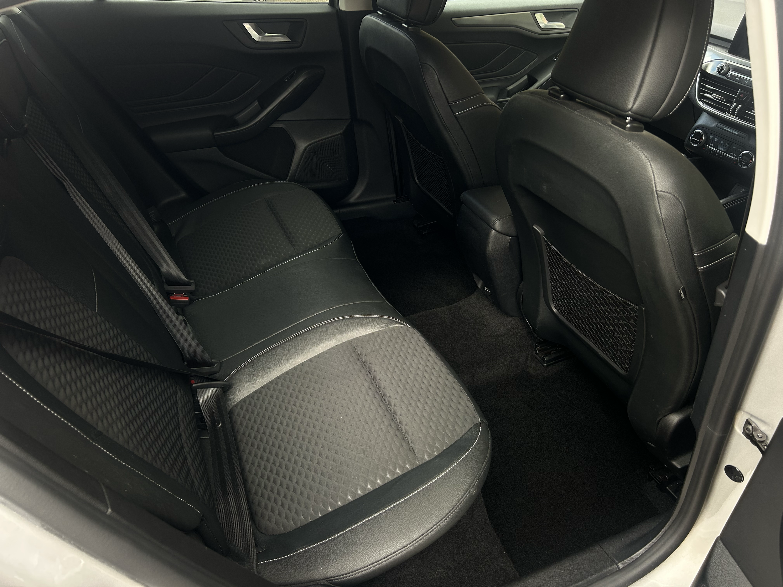 The interior of a car showing the backseat area with black and gray fabric and leather seats, door panels, and part of the dashboard.