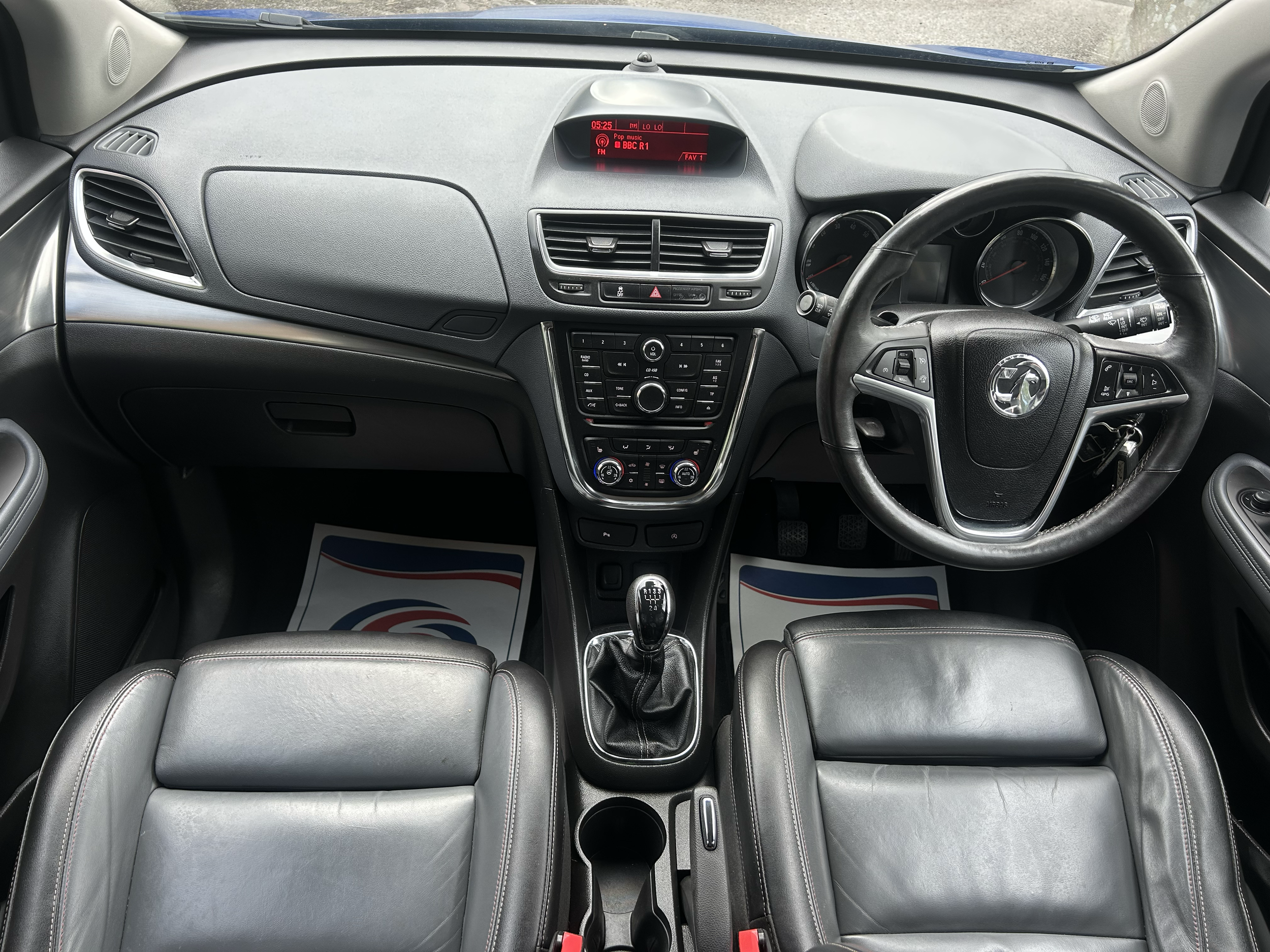 Inside view of a car's dashboard, steering wheel, gear shift, and front seats with floor mats, showing the driver's perspective.