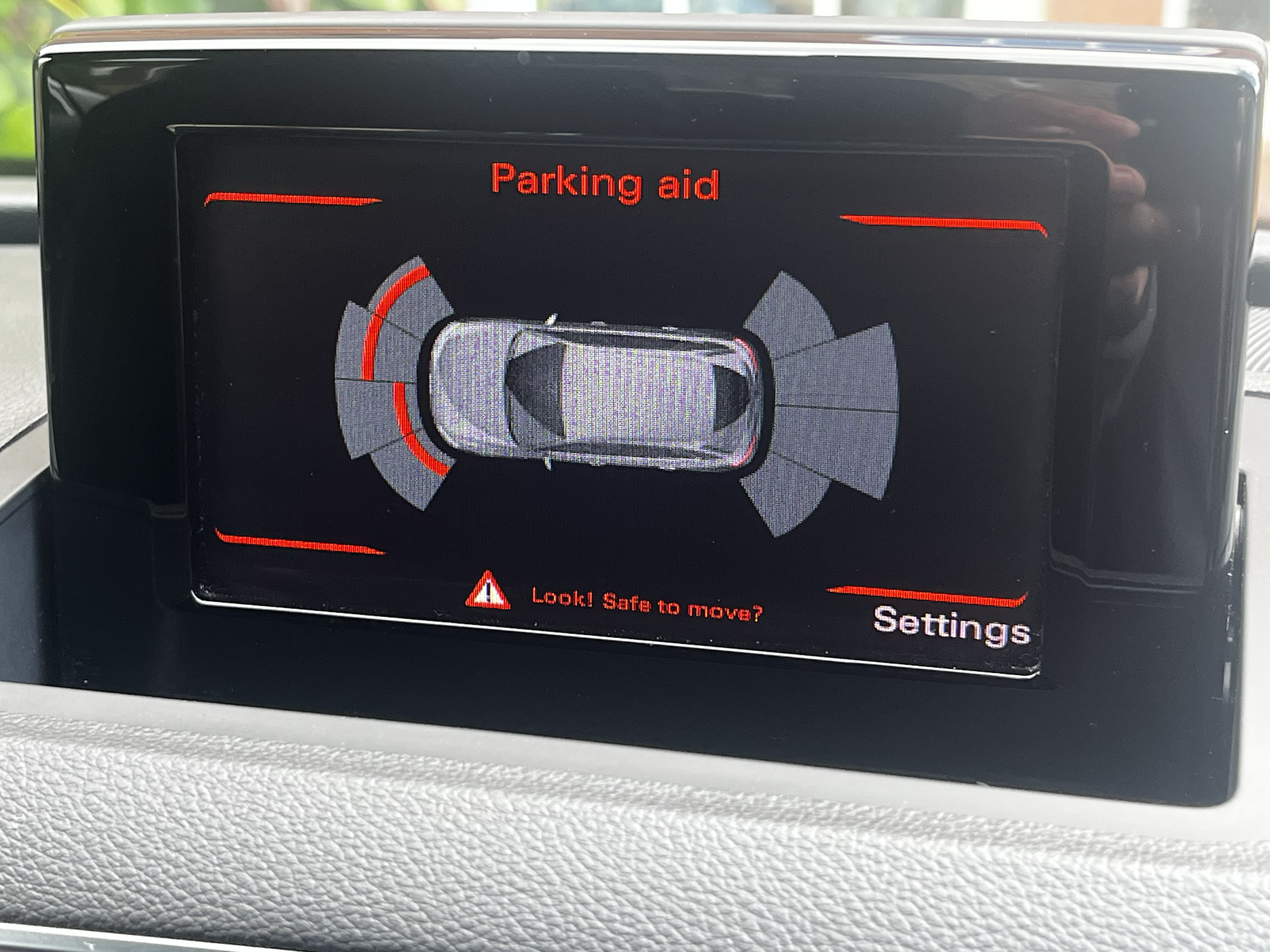 Car's parking aid display showing a top-down view of a car with surrounding sensor zones and the message "Look! Safe to move?" in red at the bottom.
