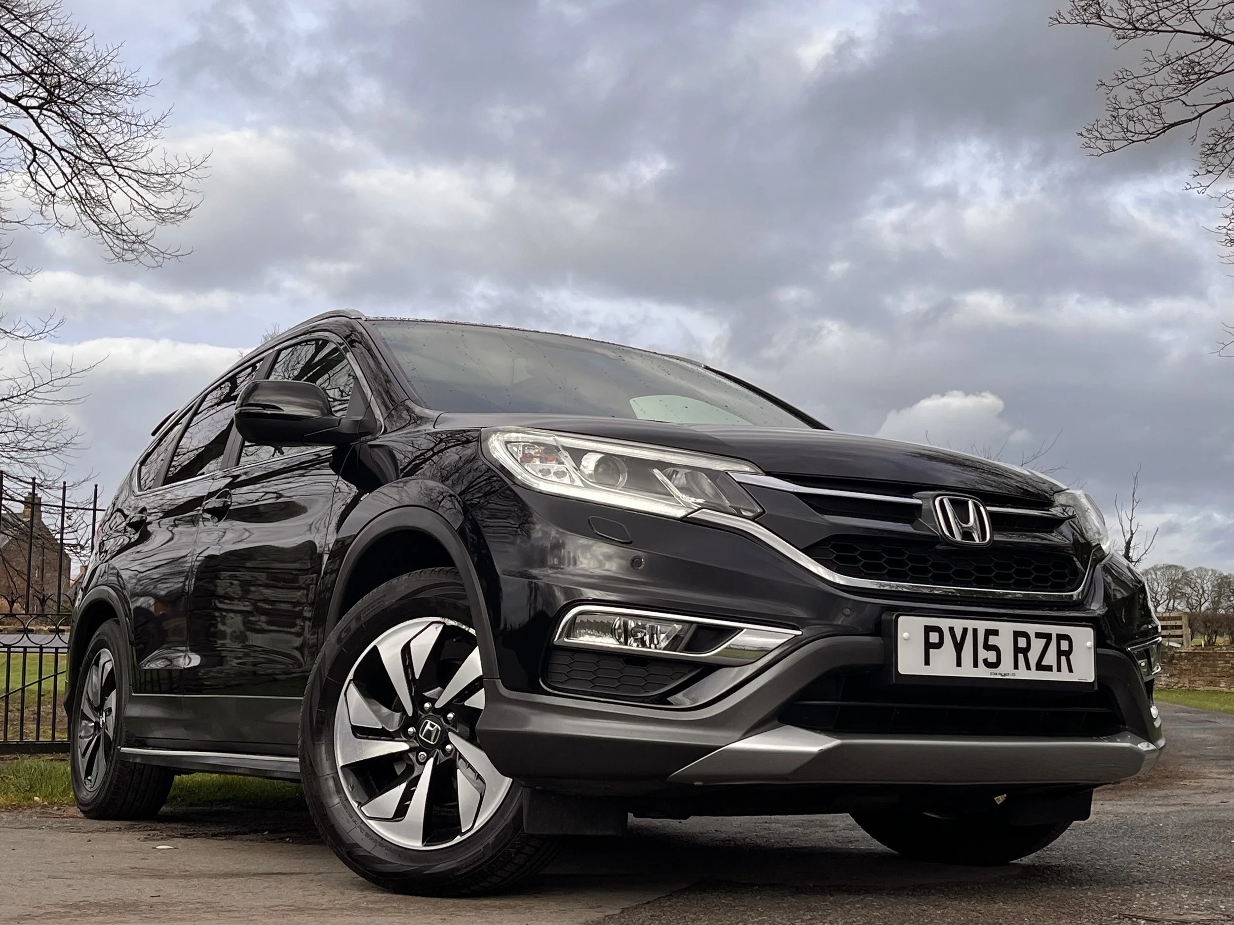 Black Honda SUV parked on a paved surface with a fenced background and cloudy sky.