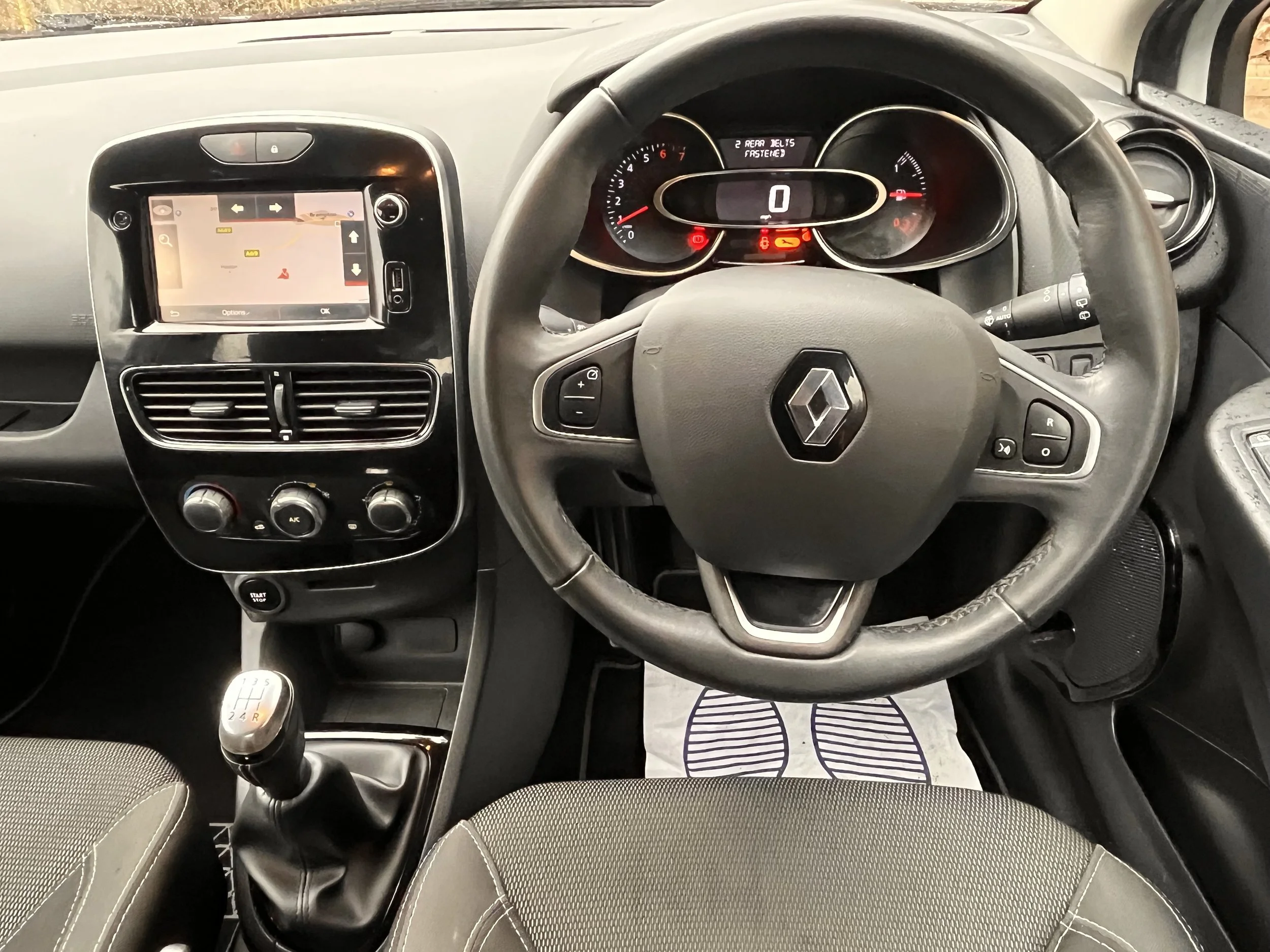 Interior of a Renault car dashboard showing steering wheel, infotainment screen, air vents, and gear shift lever.