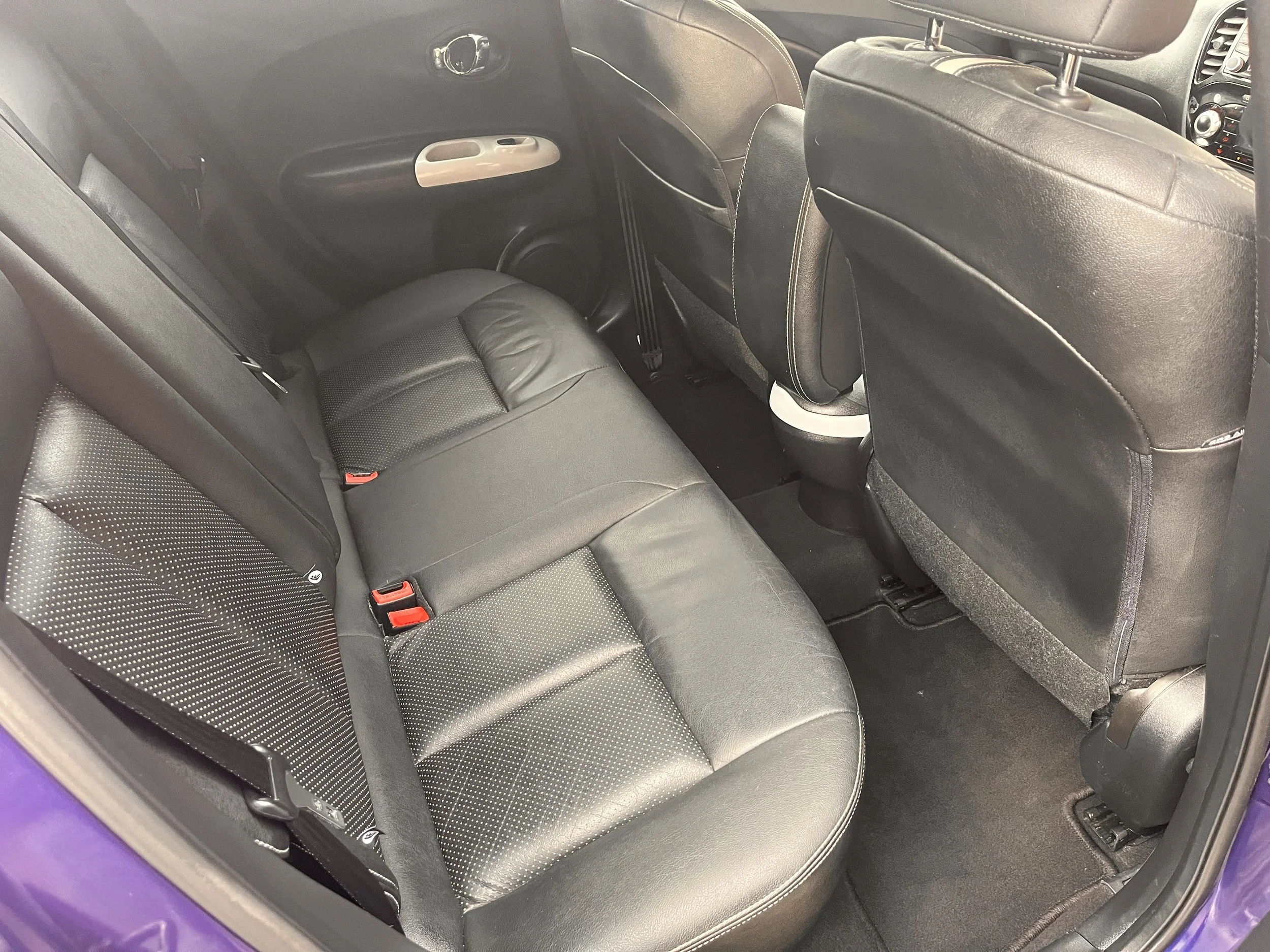 Interior of a car showing the back seats, black leather upholstery, and the backside of the front seats.