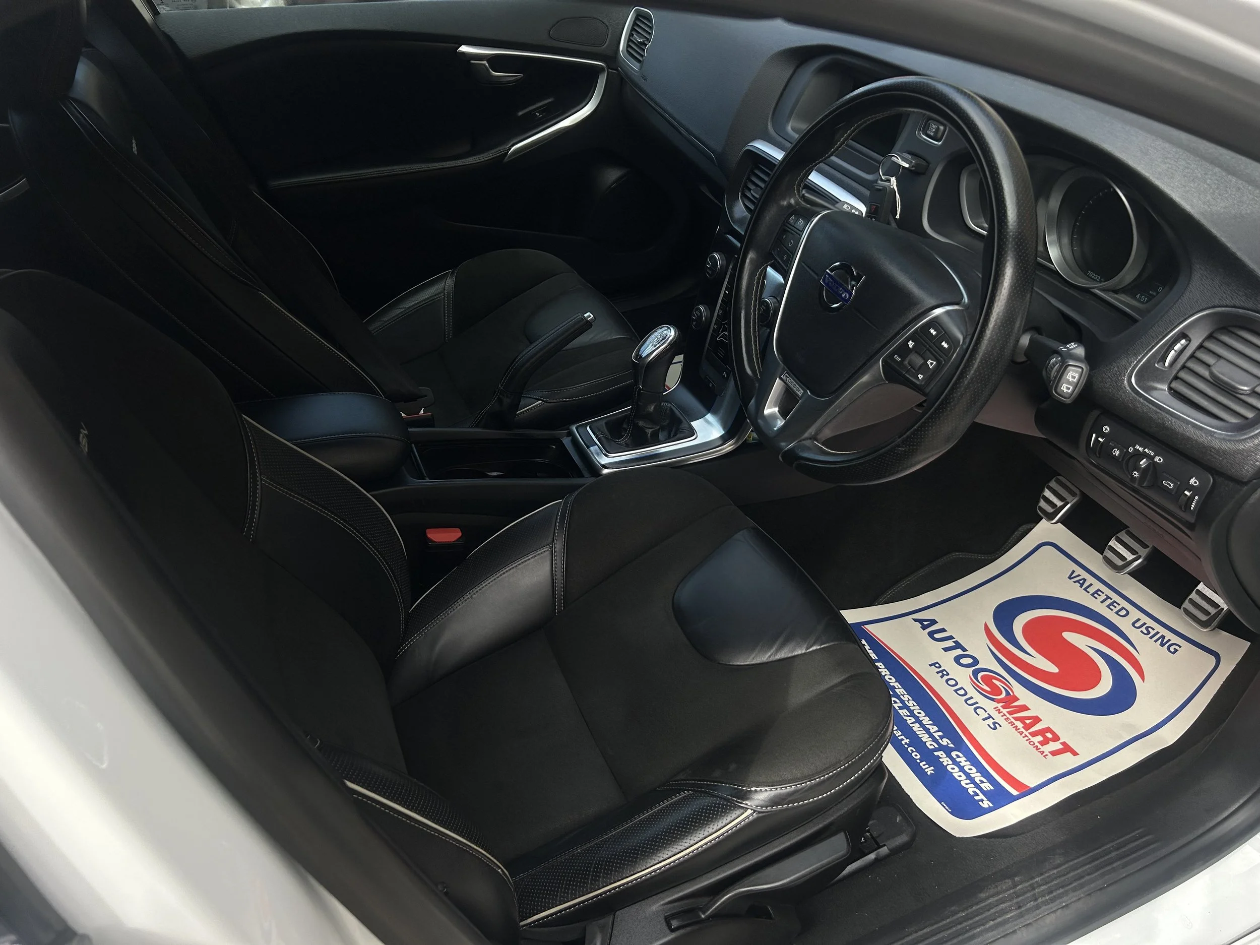 Interior of a car showing front seats, steering wheel, gear shift, and a floor mat with the logo 'AutoSmart'.
