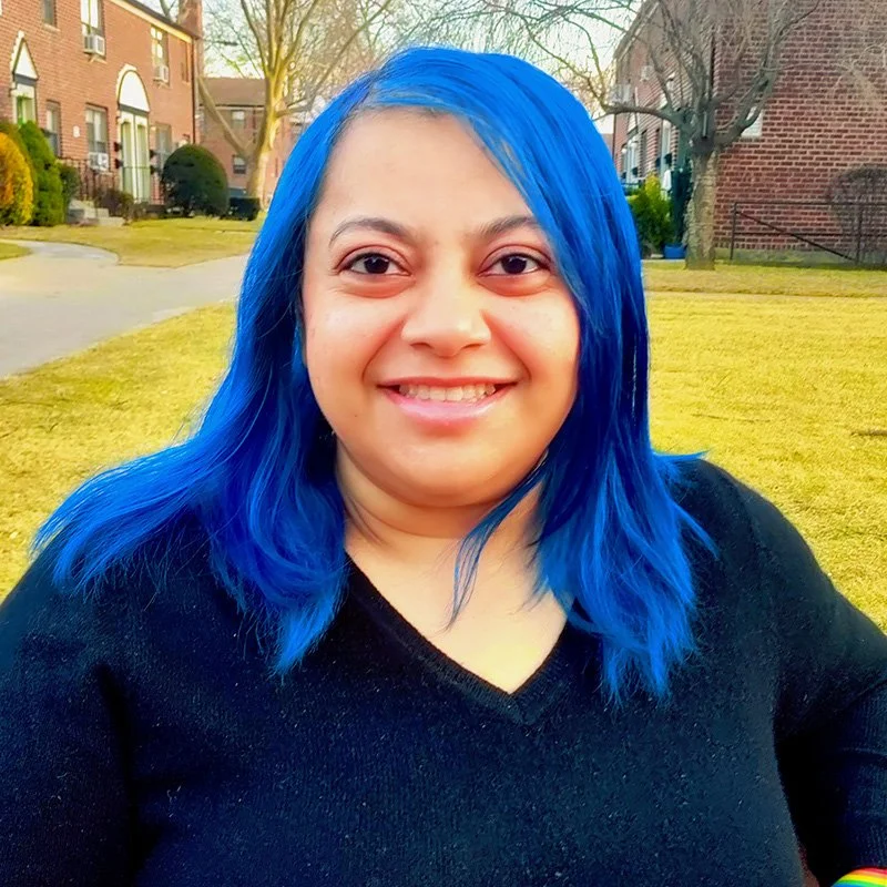 Dr. Gulshan N. Salim, trauma psychologist in New York, smiling outdoors in a black sweater with vivid blue hair — reflecting warmth, approachability, and authenticity.