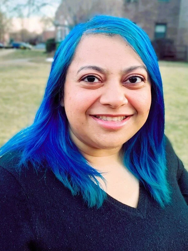 Dr. Gulshan N. Salim, Psy.D., smiling with vibrant blue hair outdoors — a trauma therapist who shows up authentically for high-achieving adults in New York.