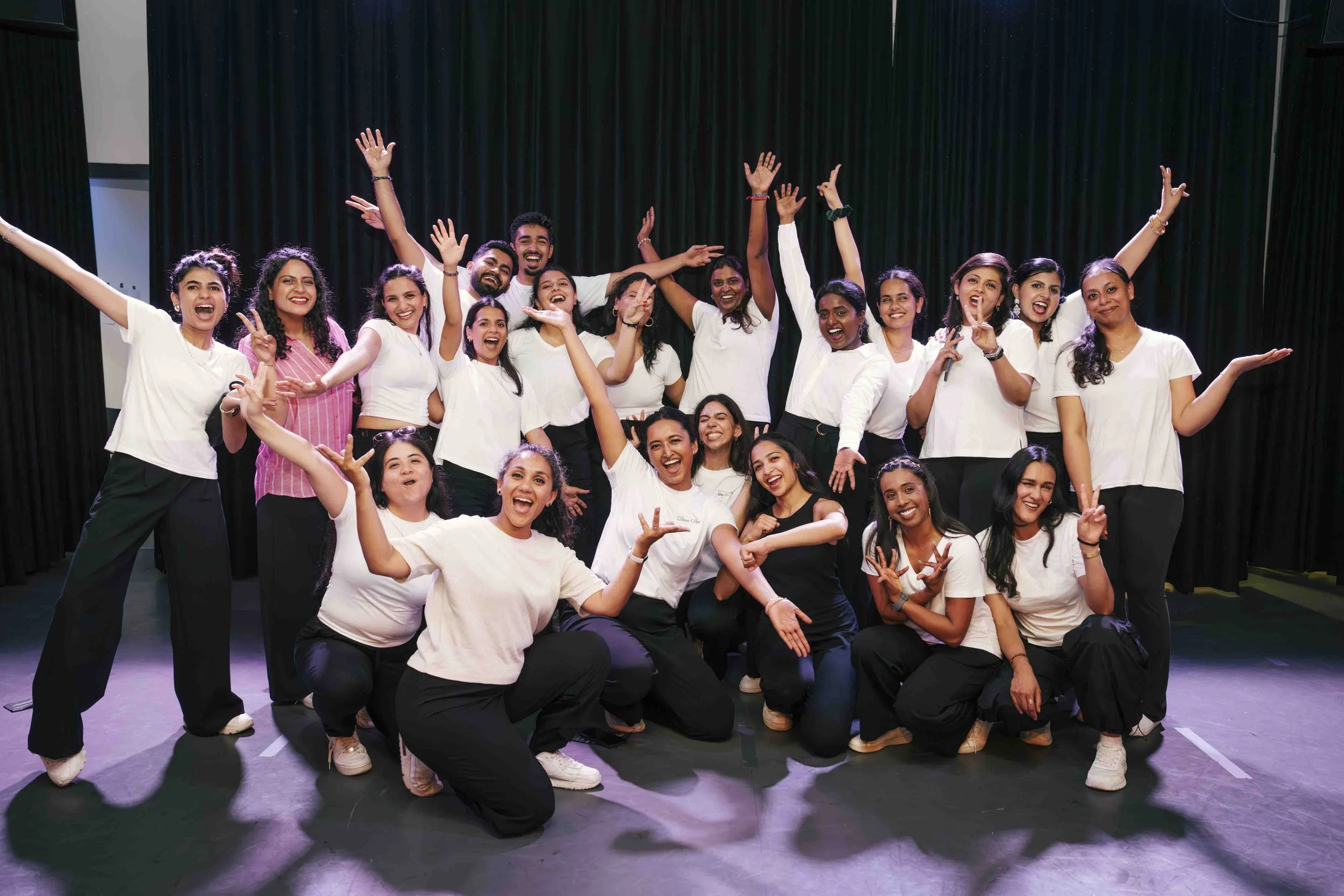 Group of people on stage celebrating, some with arms raised and smiling, against a black curtain background.
