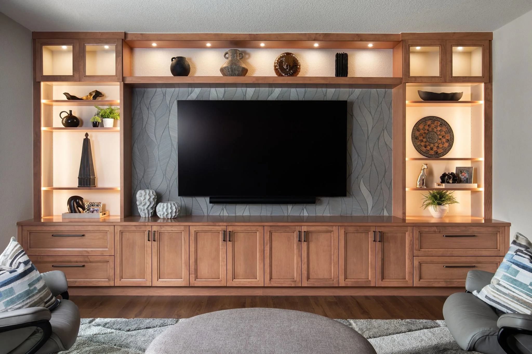 Living room with built-in wooden entertainment center, a large flat-screen TV, decorative items on shelves, and two armchairs with striped pillows.