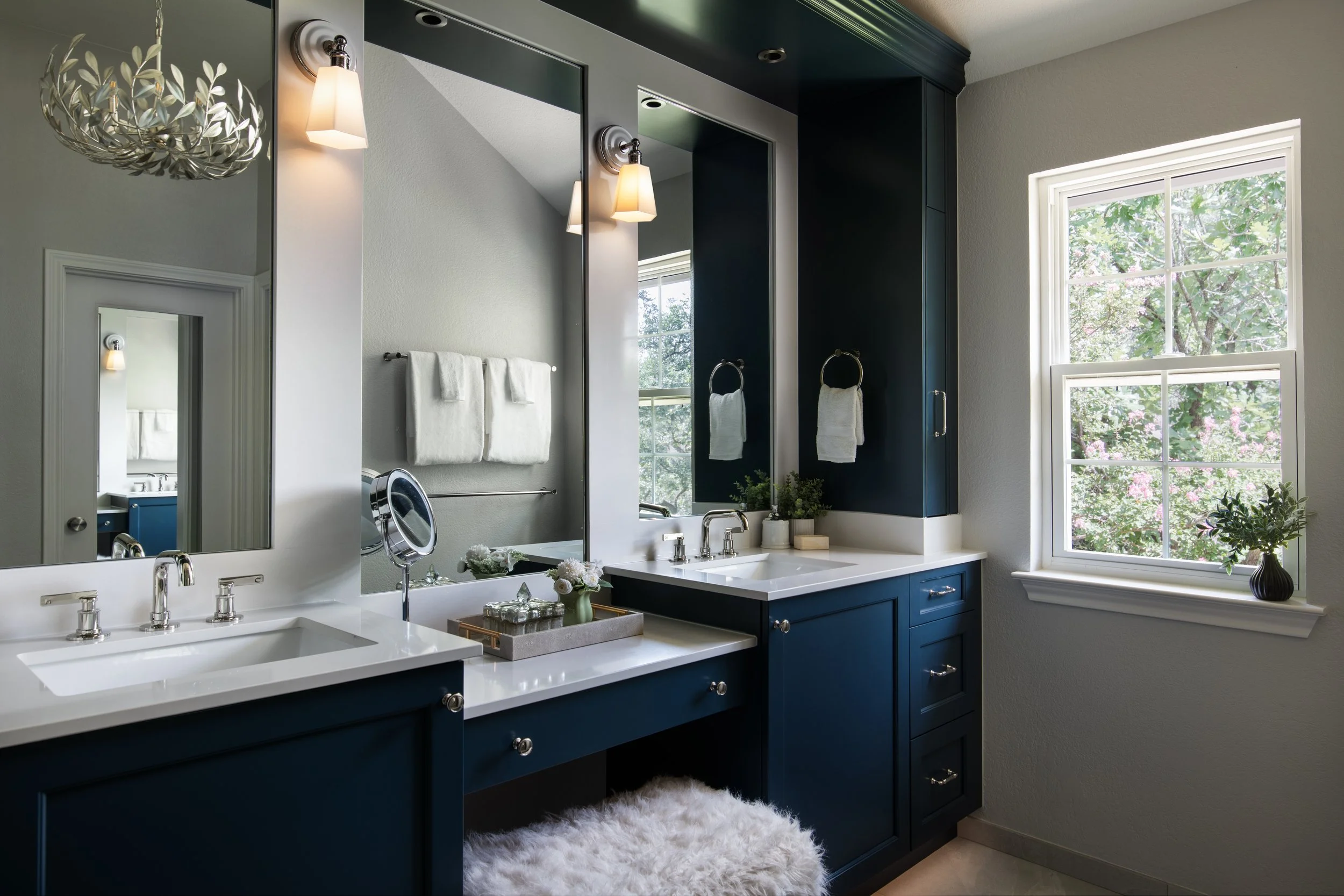 Modern kitchen with white cabinets, dark island, marble countertops, geometric pendant lights, and bar stools. Large windows offer garden views.