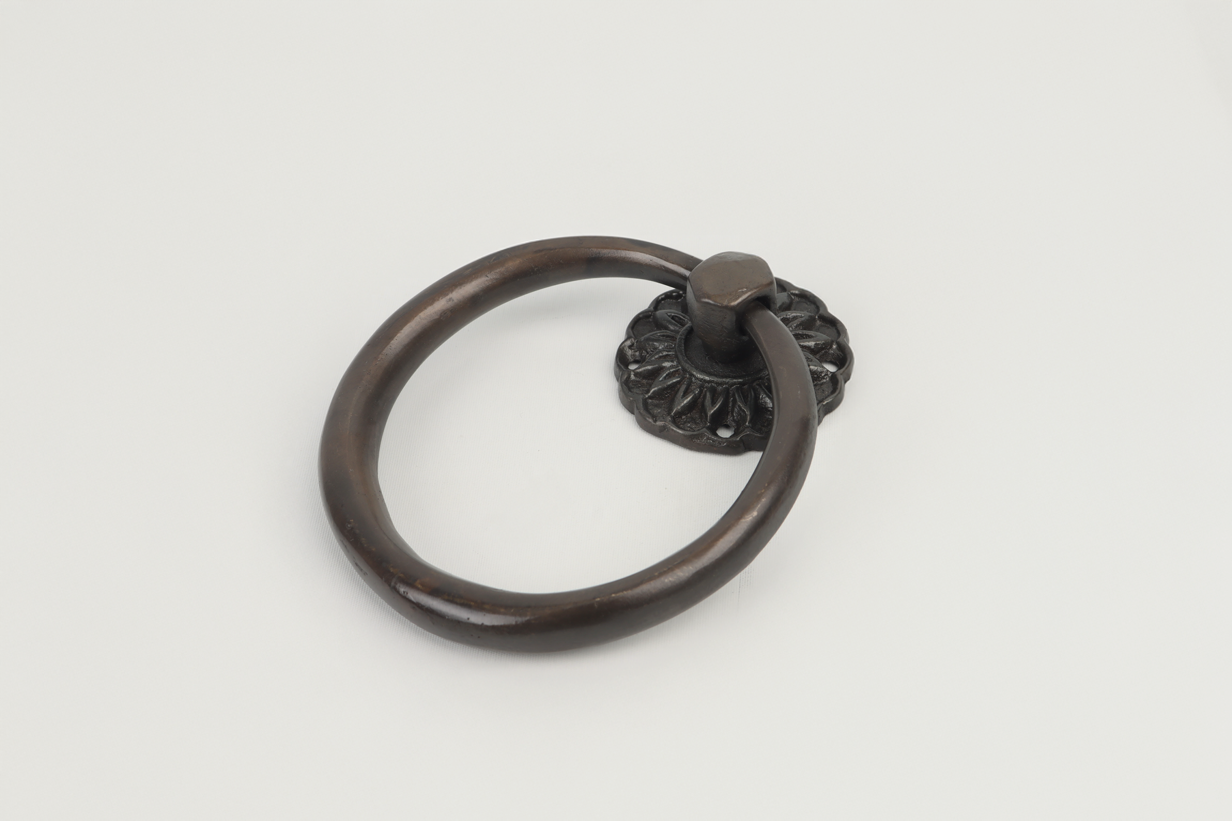 Metal door knocker with a circular ring and decorative backplate, placed on a white surface.