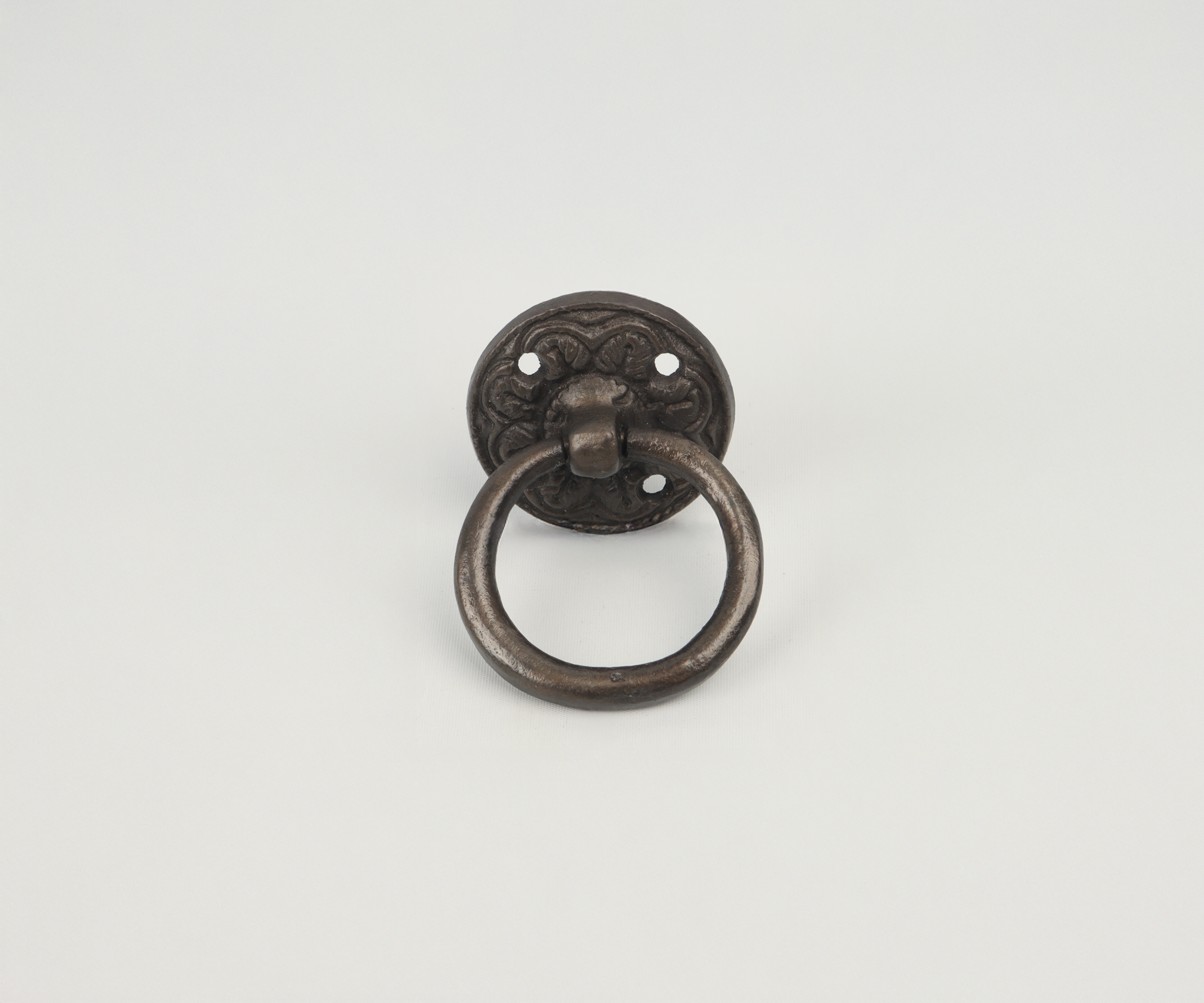 A vintage dark metal door knocker with an ornate circular backplate and a large ring handle, centered on a white background.