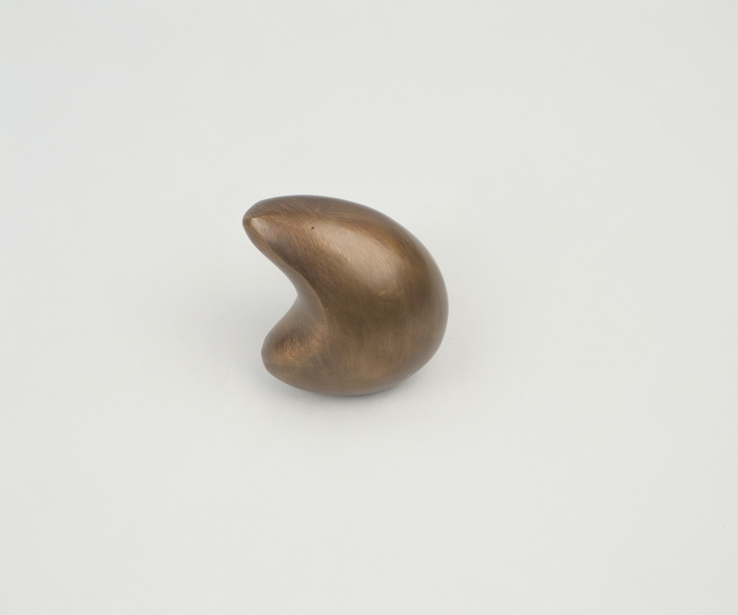 A small, smooth, bronze-colored sculpture resembling a kidney bean on a white background.