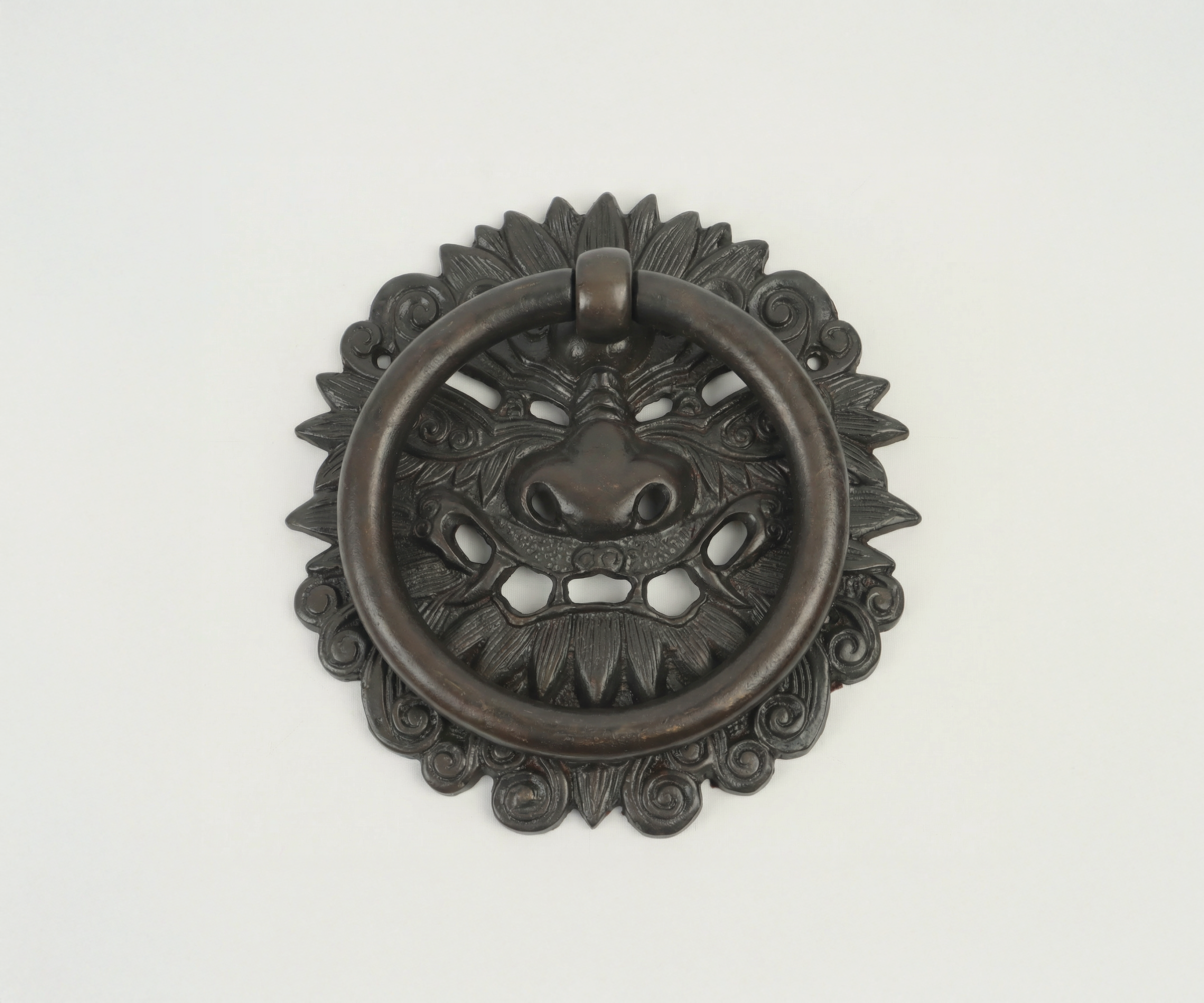 Decorative metal door knocker with a lion's face and a ring, mounted on a white background.