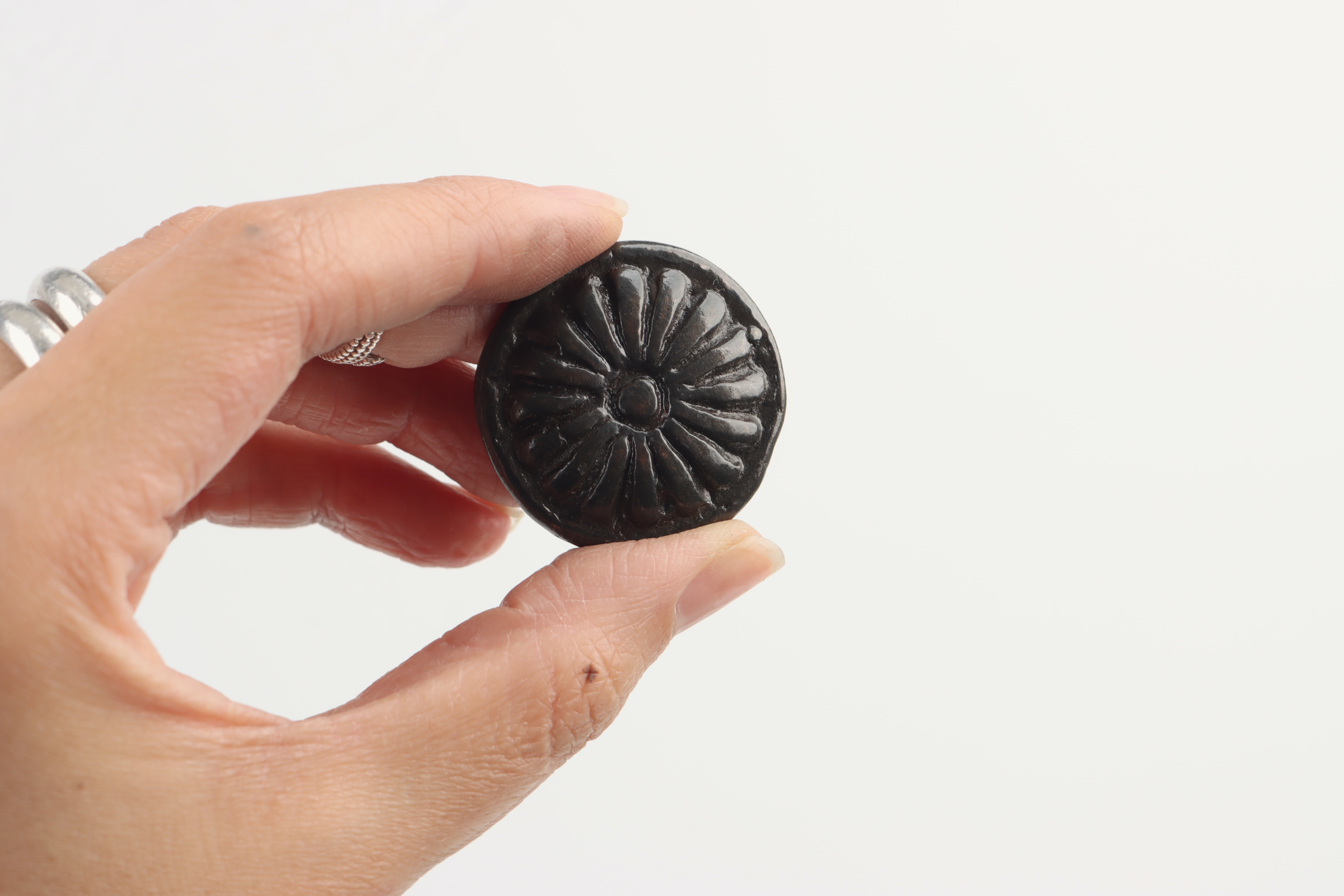 Person holding a small, round, black object with a floral design on a white background.