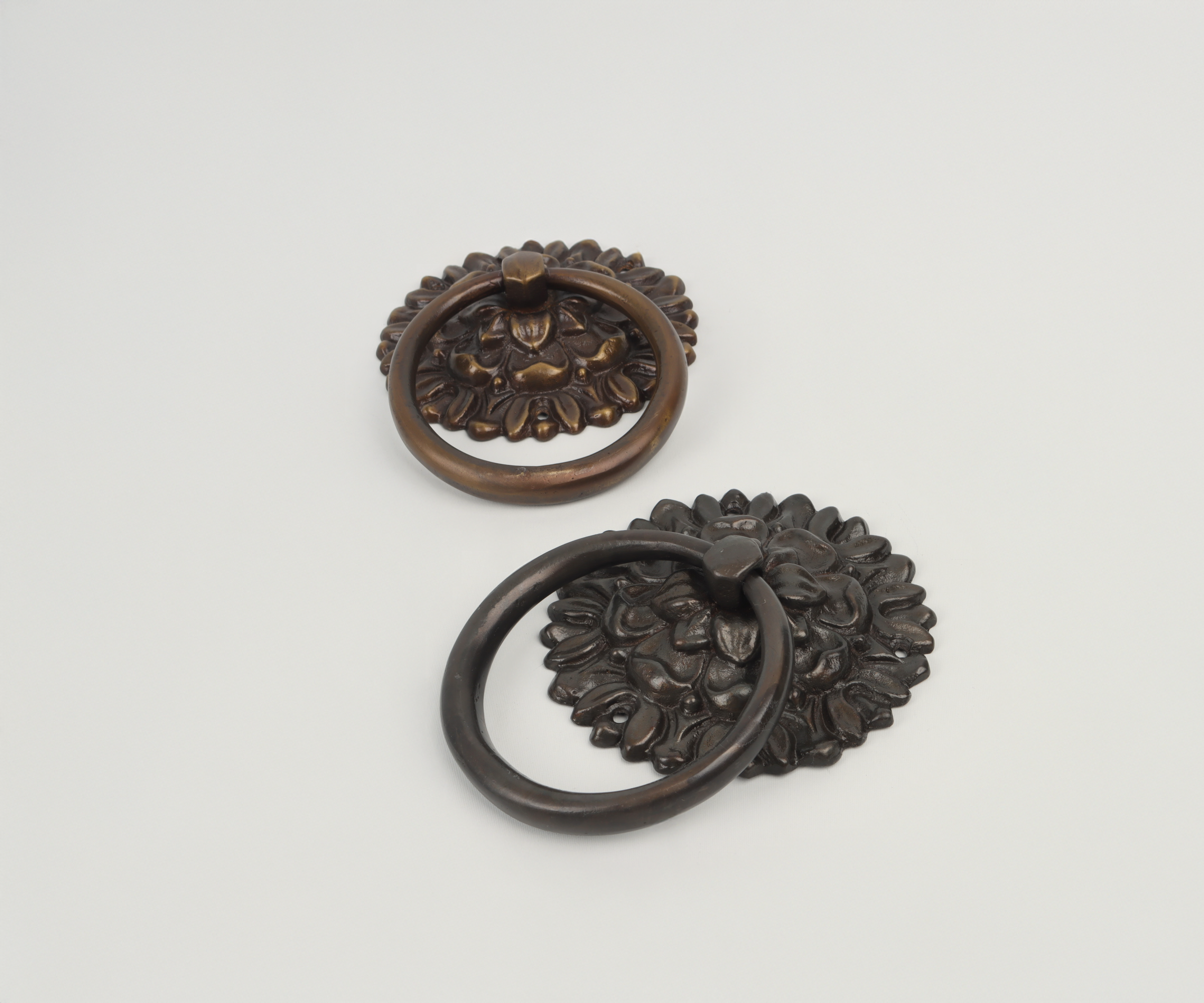 Two decorative metal door knockers with floral designs, one in bronze and one in black.