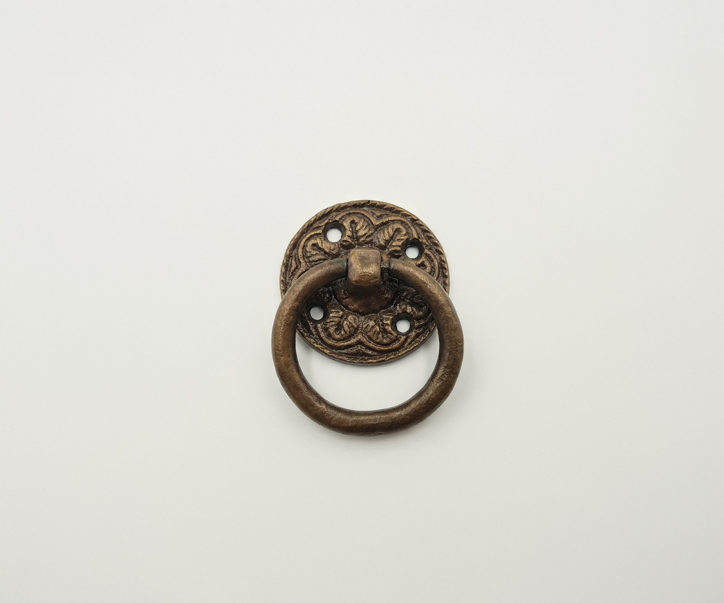 A vintage brass door knocker with an ornate circular backplate and a round ring handle, mounted on a plain white surface.
