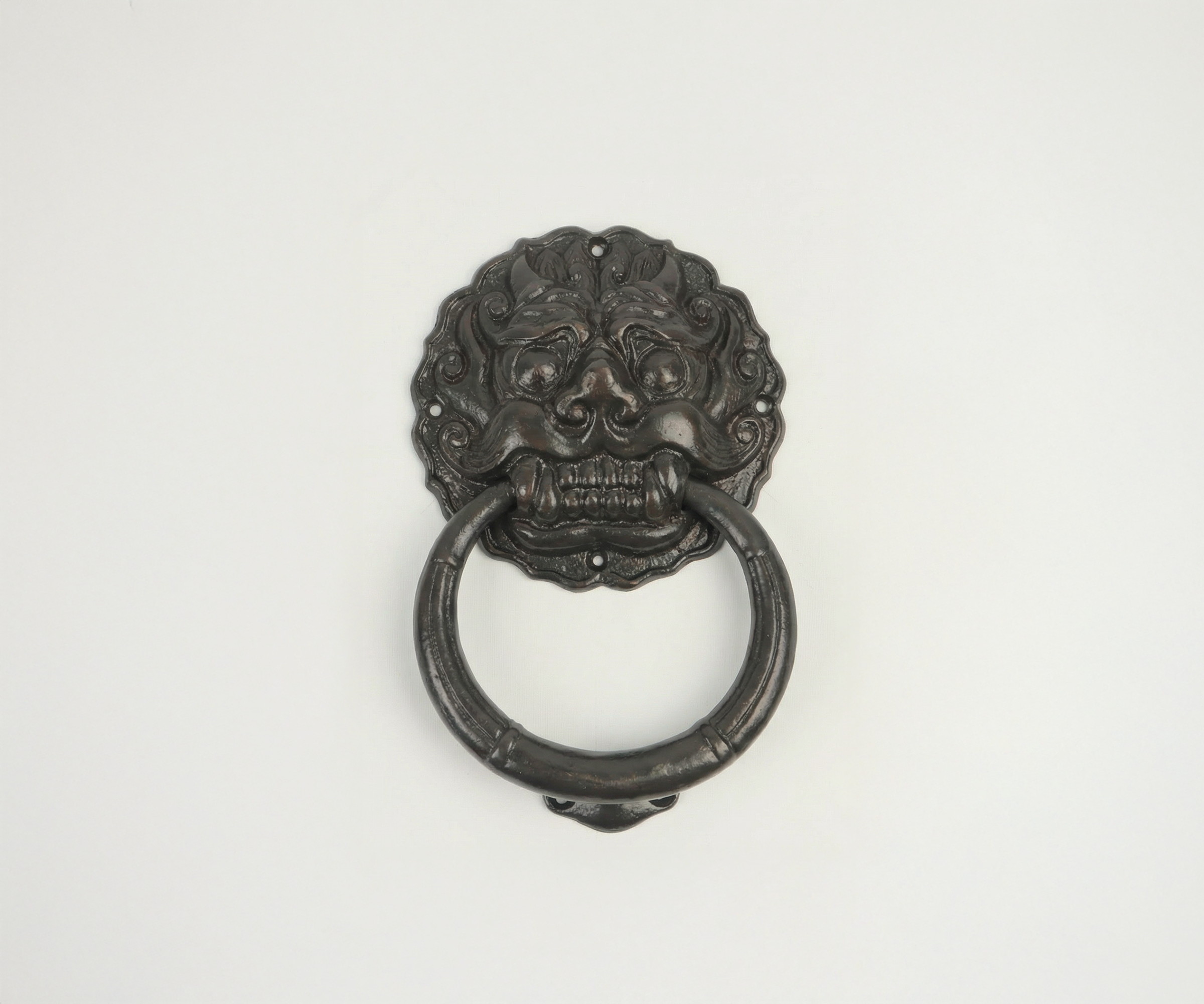 Decorative black door knocker featuring a lion's face with a ring in its mouth, mounted on a white wall.