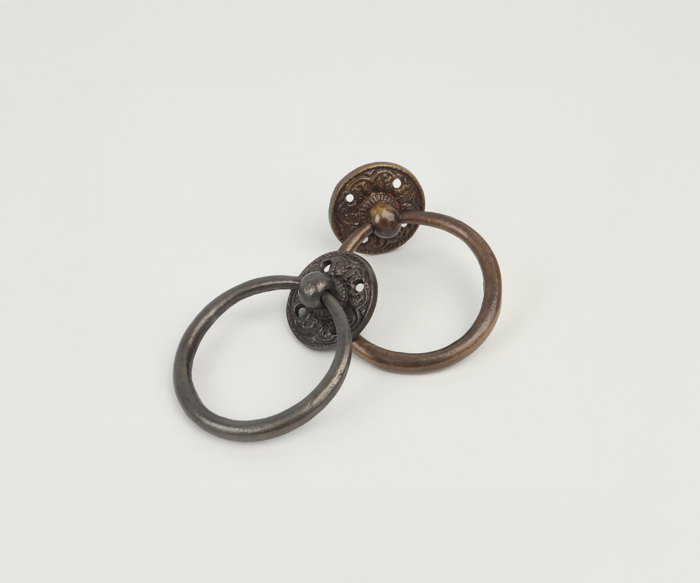 Two antique cast iron wall hooks with circular bases and ring handles mounted on a white surface.