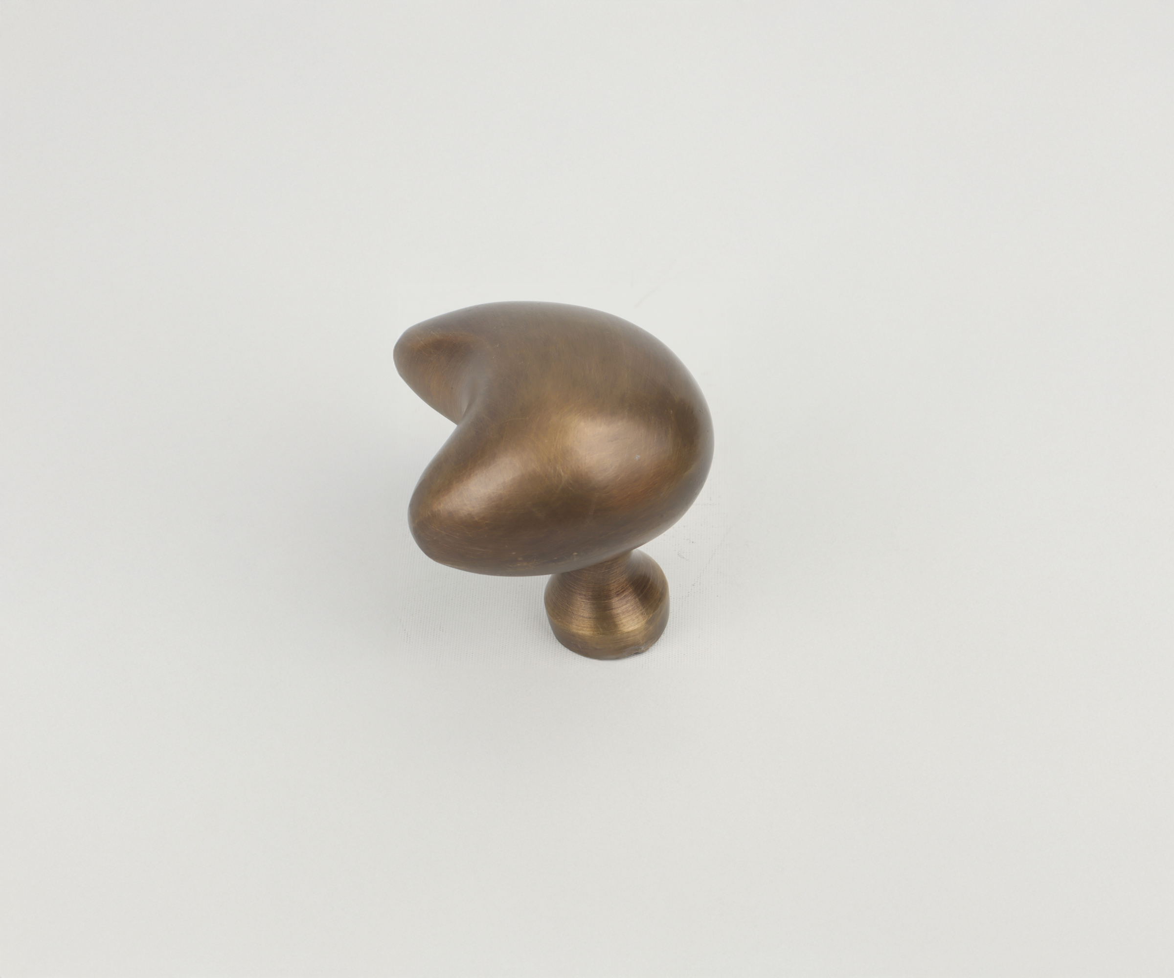 A small, abstract bronze sculpture with a spherical base and an irregularly-shaped top on a white surface.