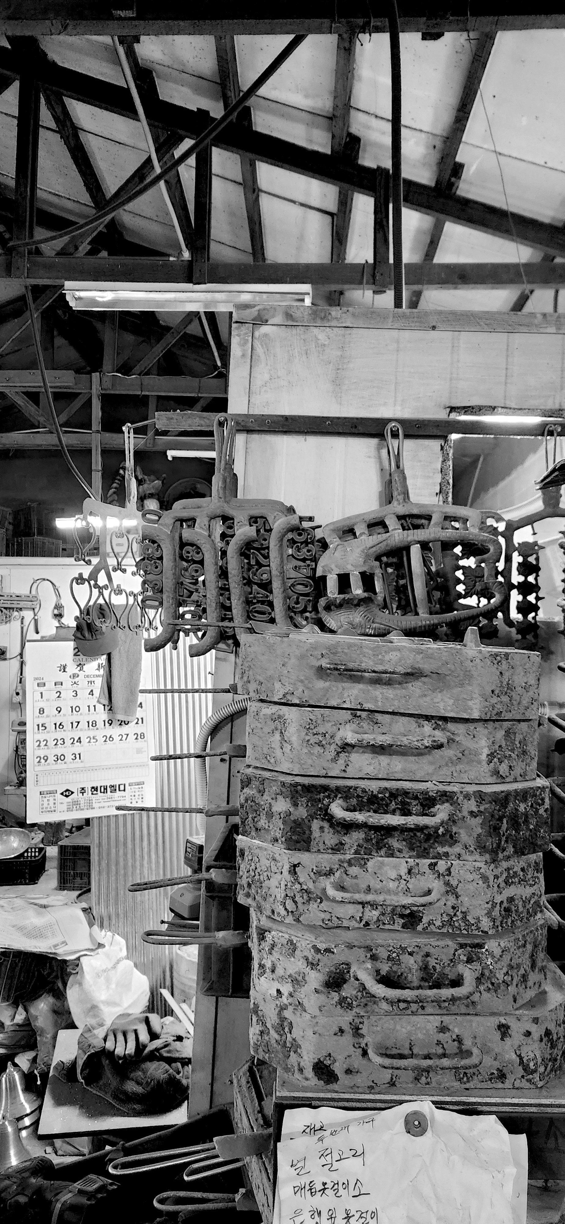 Old rusty padlocks and chains hanging on a rack in a cluttered workshop with a calendar, various tools, and shelves in the background.