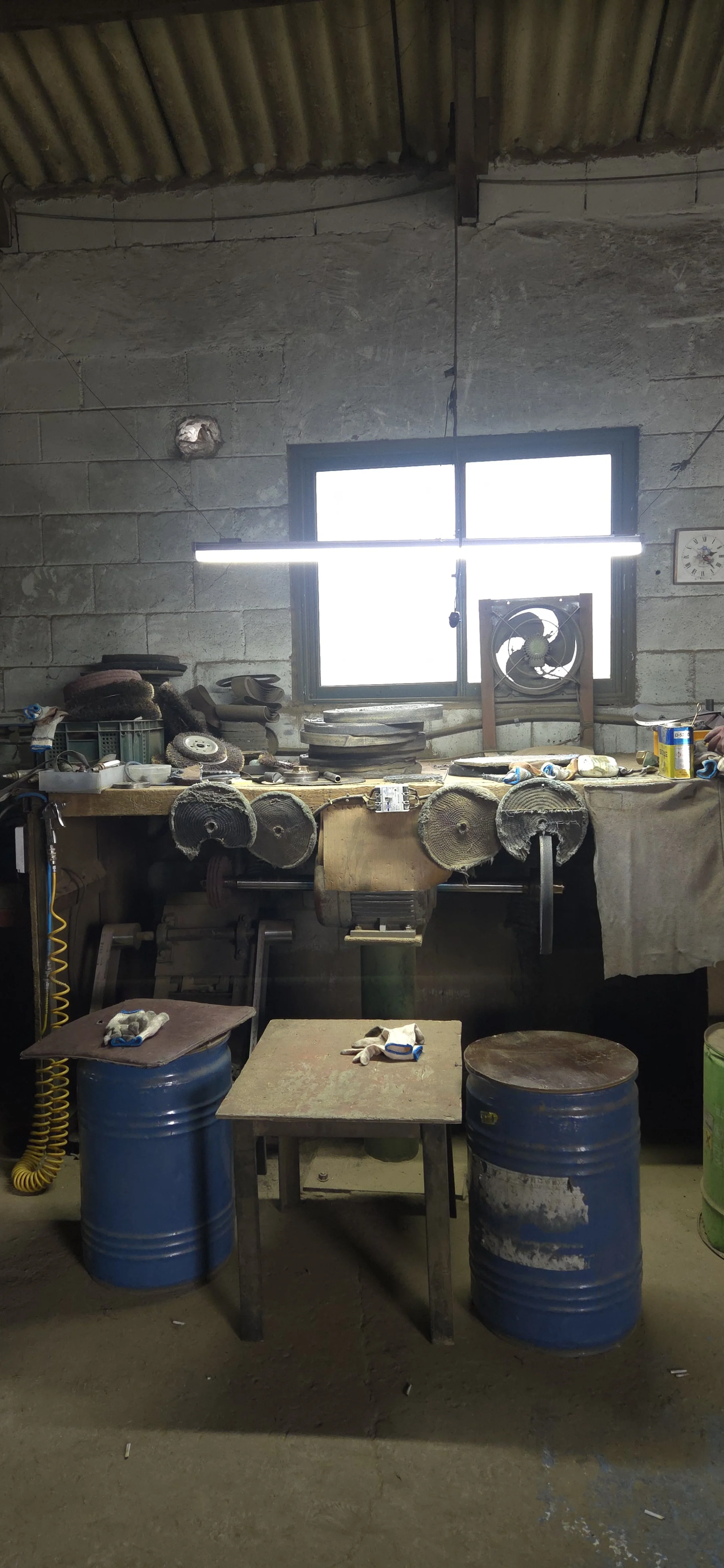 A workshop with a wooden workbench and tools, industrial space with concrete walls, a window, and work gloves on a small table below.