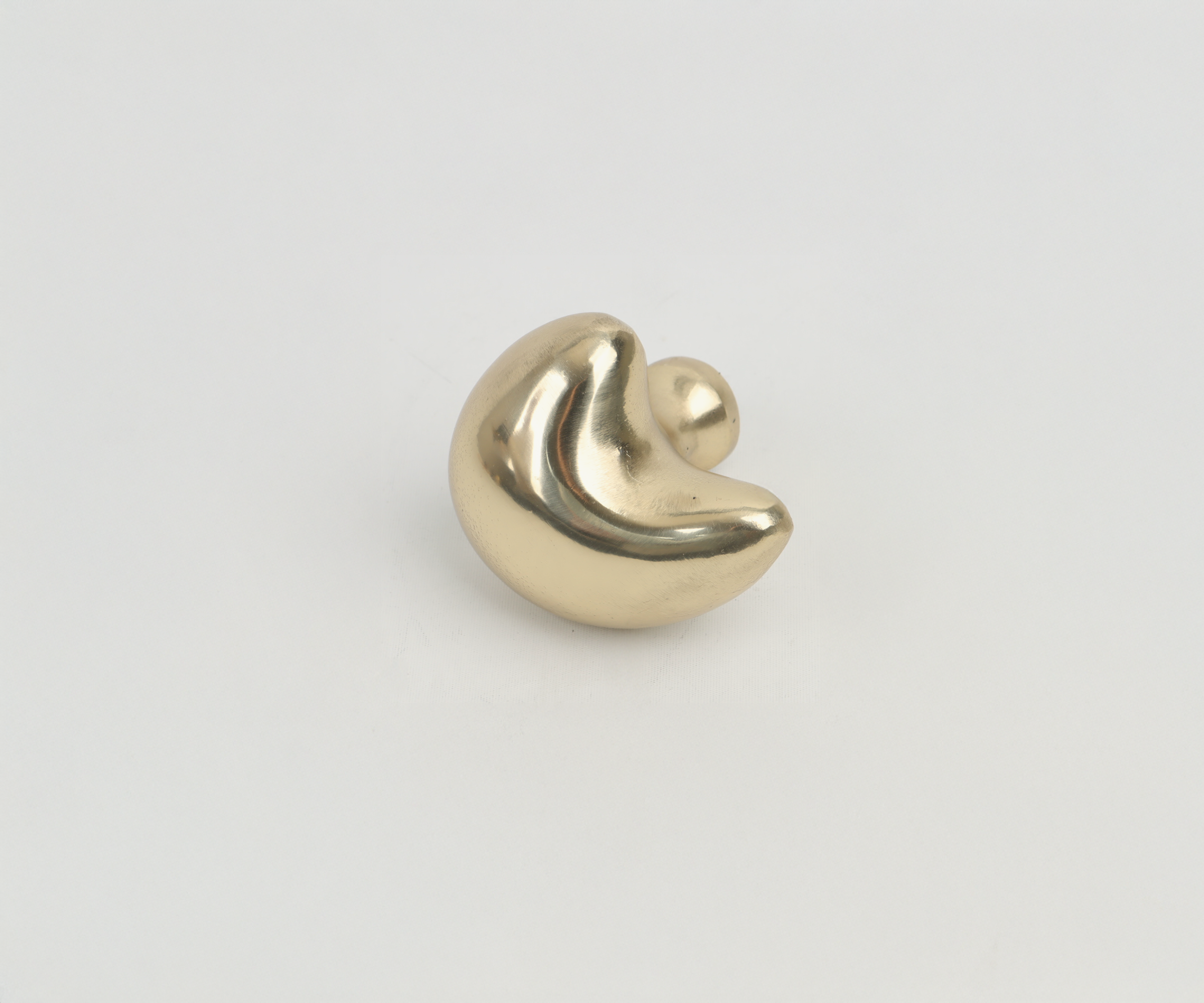 A gold-colored, abstract metallic sculpture with smooth, curved shapes on a white background.