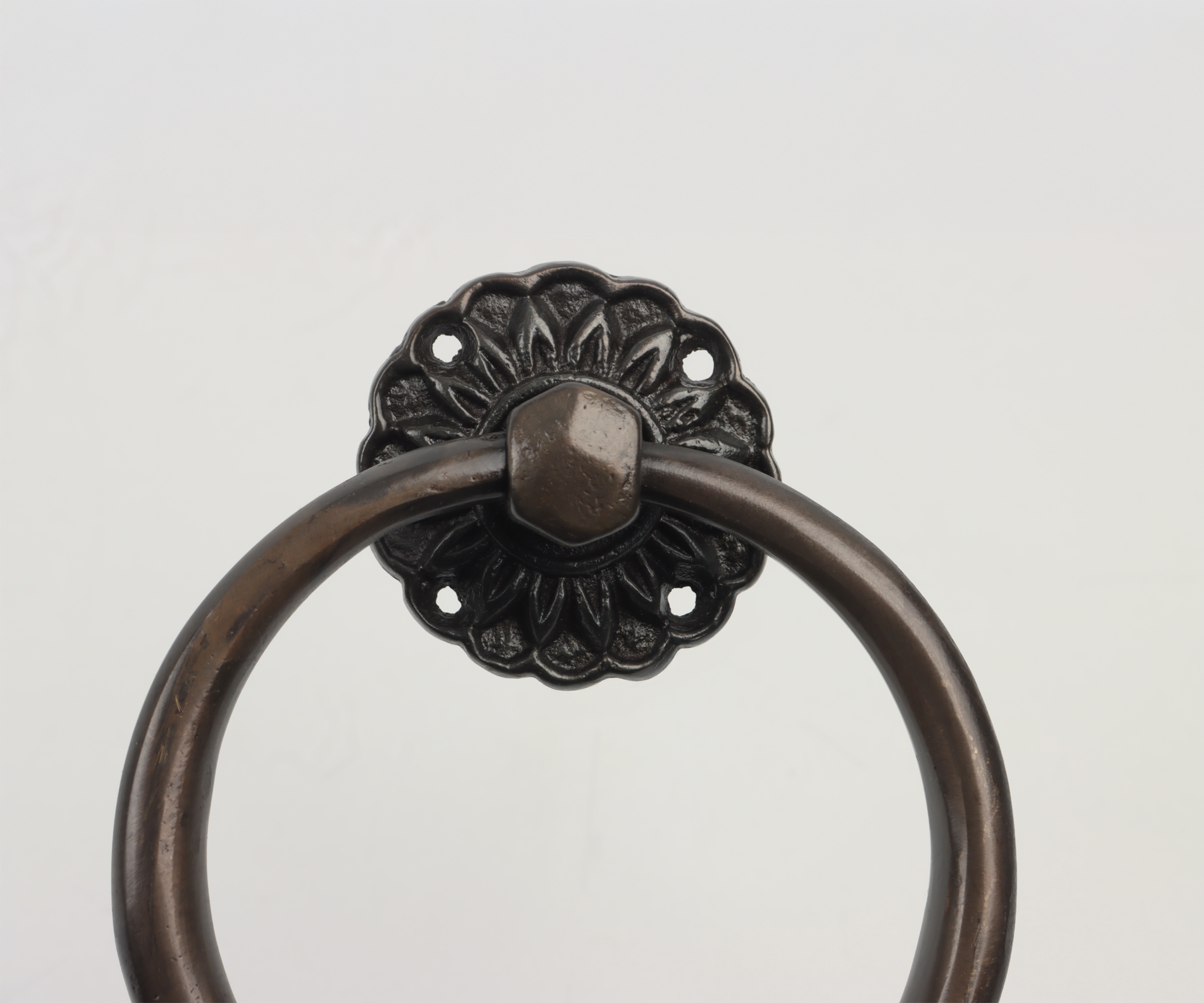 Close-up of a vintage metal towel ring with a decorative black backing on a white wall.