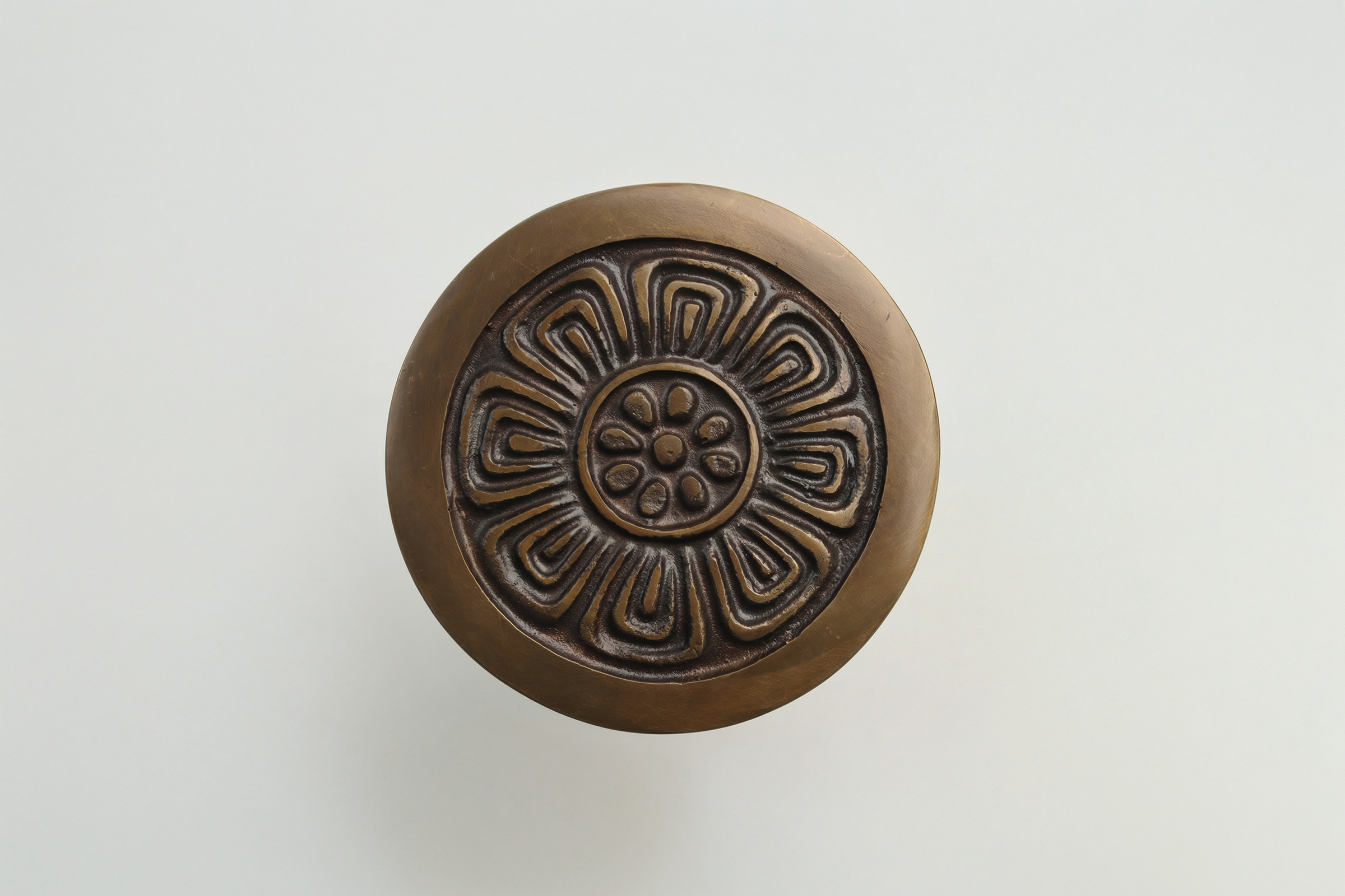 Round decorative object with an intricate spiral pattern on a plain light background.