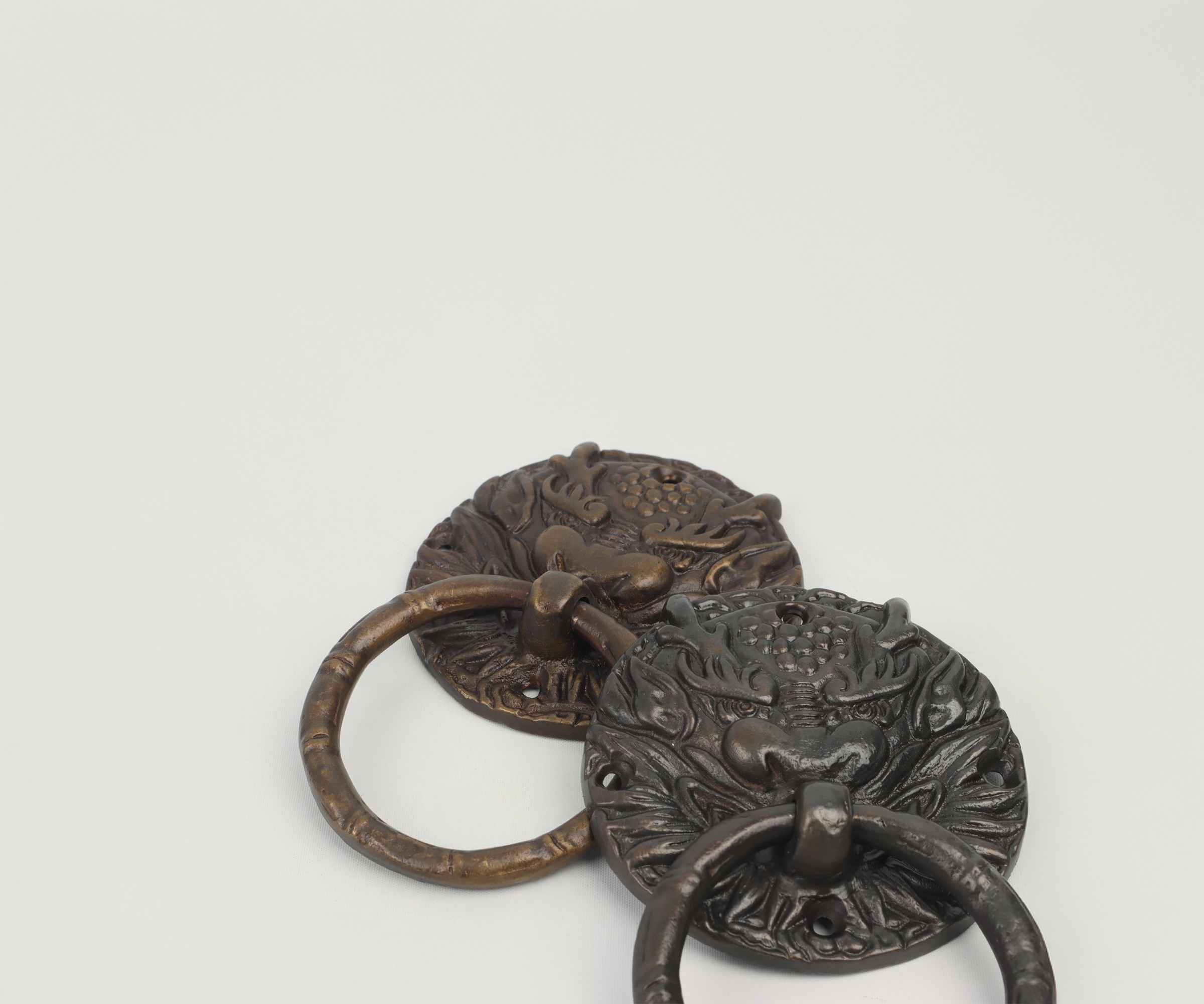 Two ornate metal door knockers with lion faces and decorative patterns, one brass and one dark metal, on a plain white background.