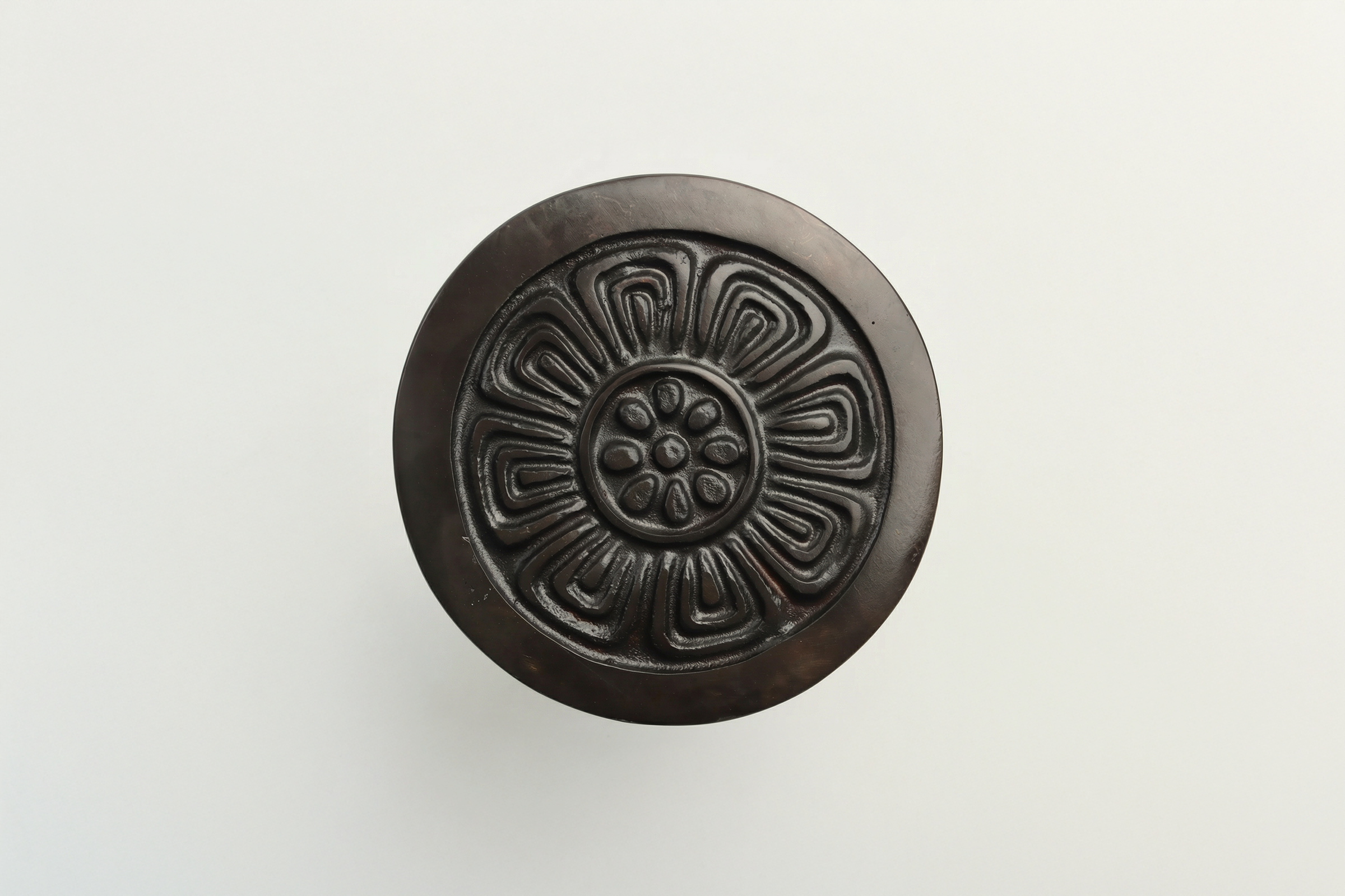 Top view of a circular decorative black object with intricate floral or geometric patterns on a white background.