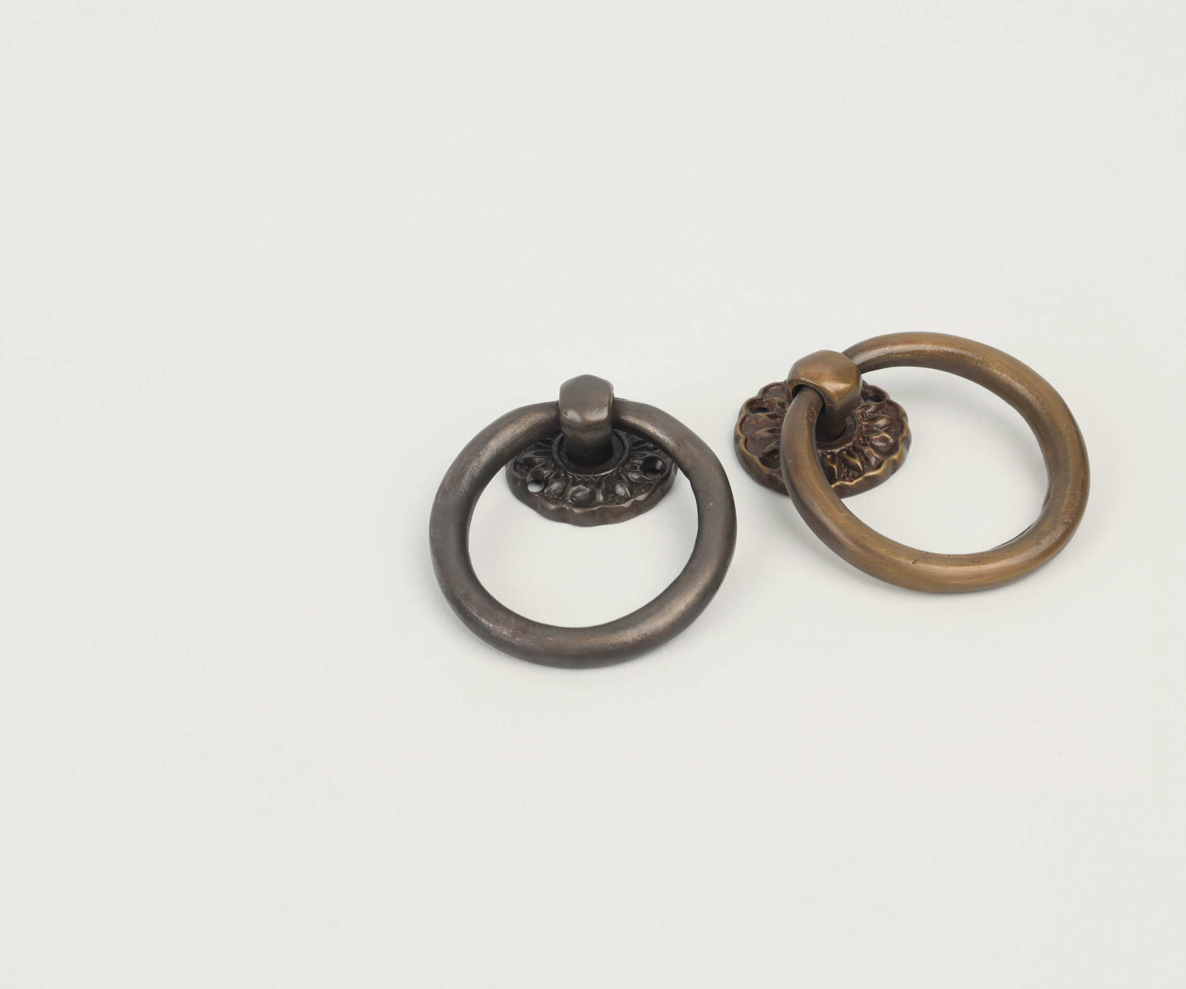Two circular metal door knockers, one dark bronze and one brass, laying on a white surface.