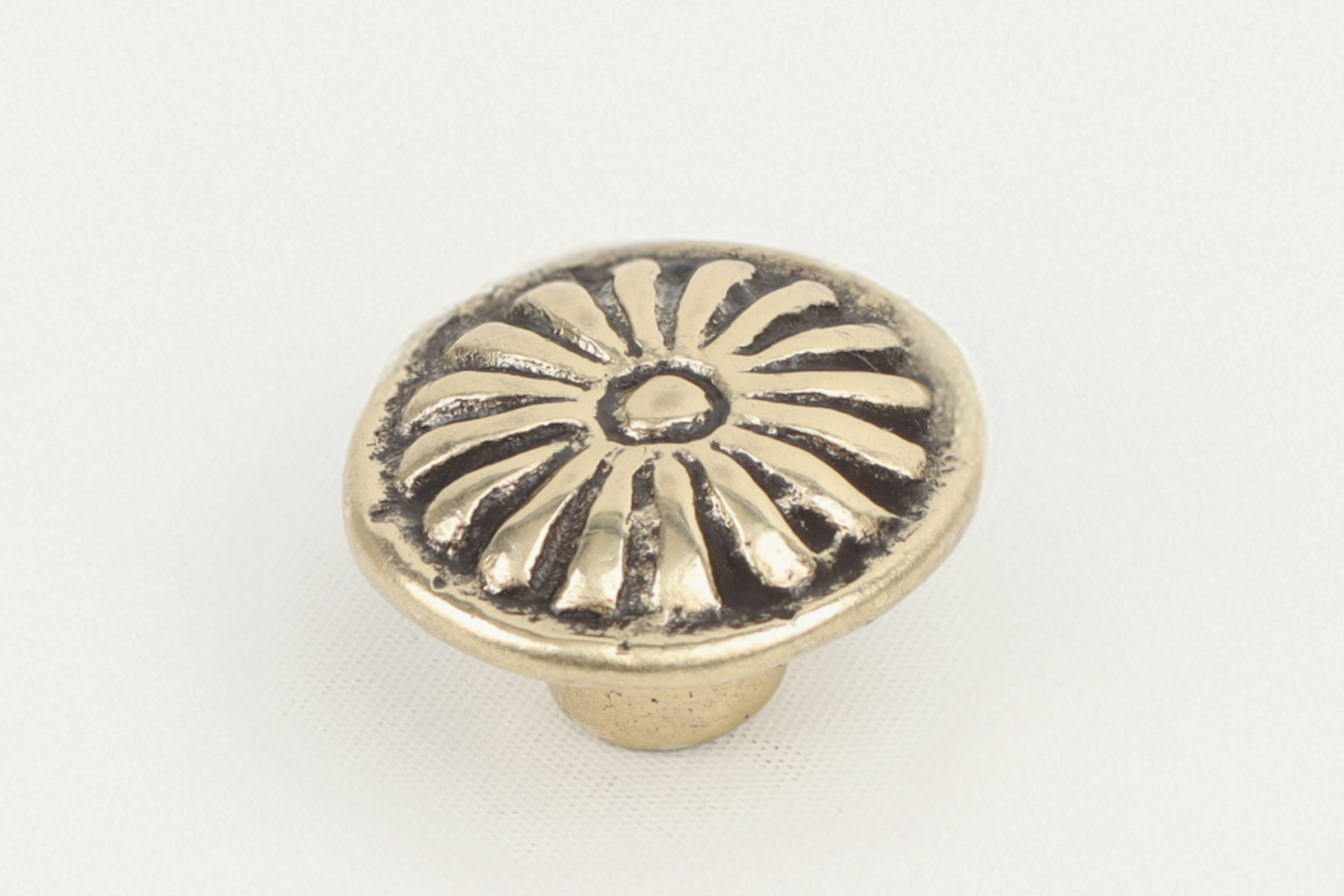 A shiny, gold-colored round cabinet knob with an intricate floral or sunburst design on the top surface, set against a plain light background.