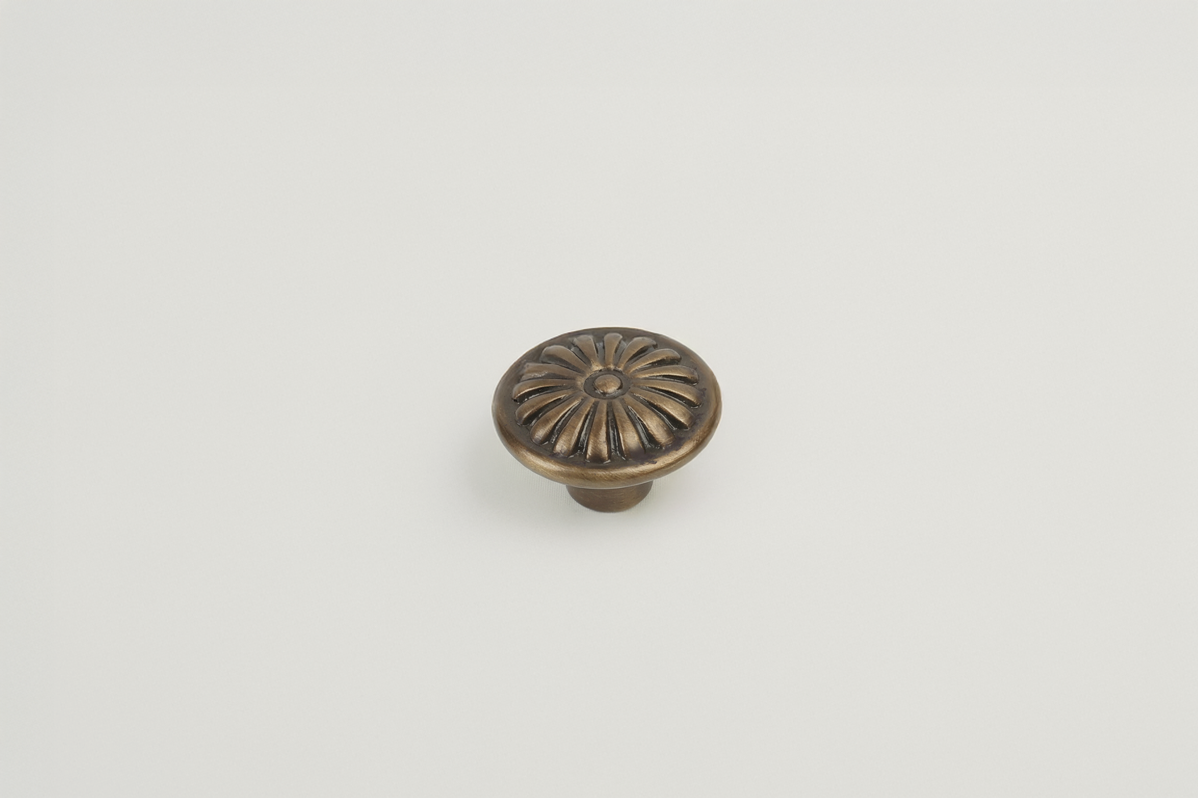 Decorative bronze-colored drawer or cabinet knob with floral pattern on a plain, white surface.