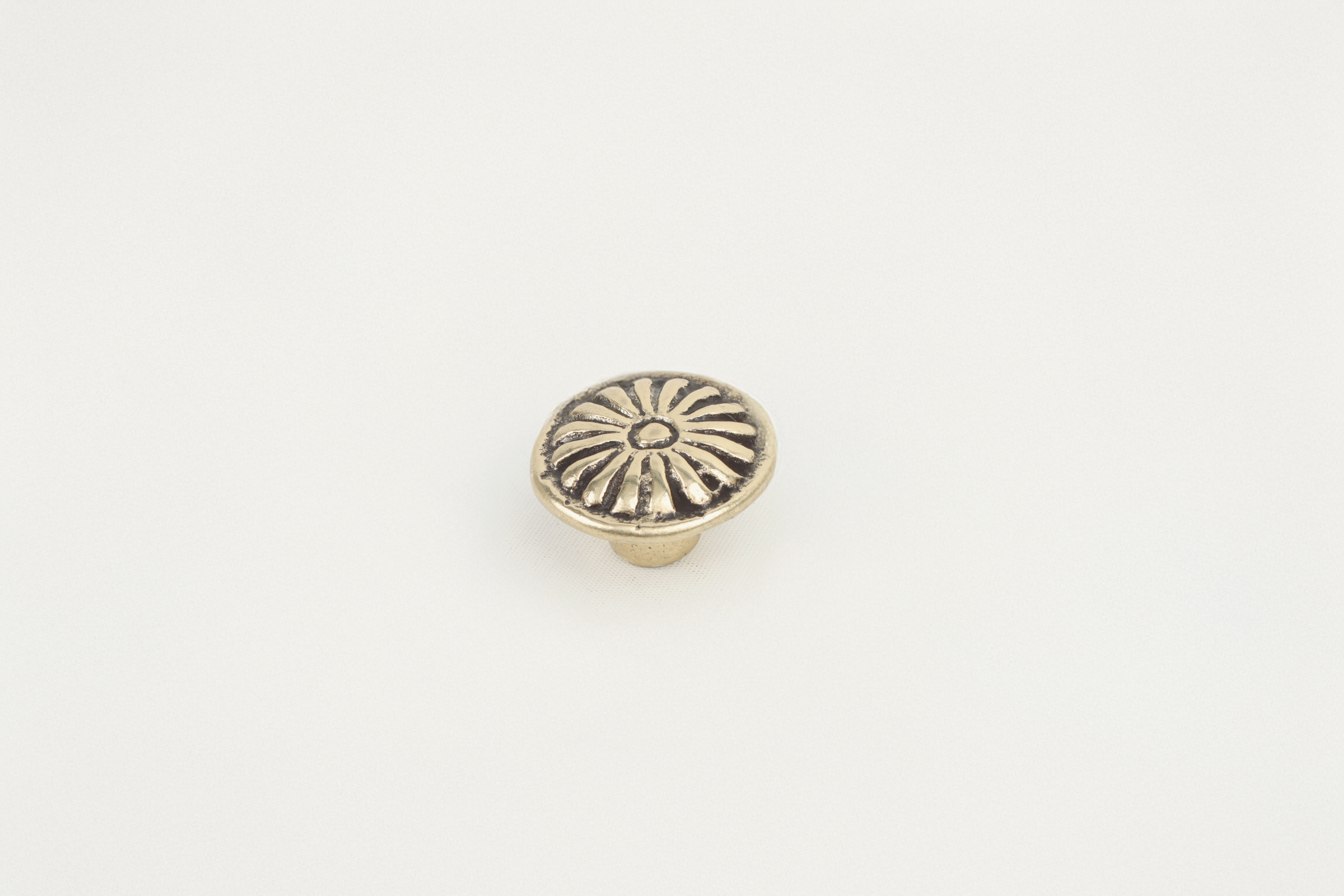 A small, round metallic decorative object with a floral or sunburst pattern, placed on a white background.