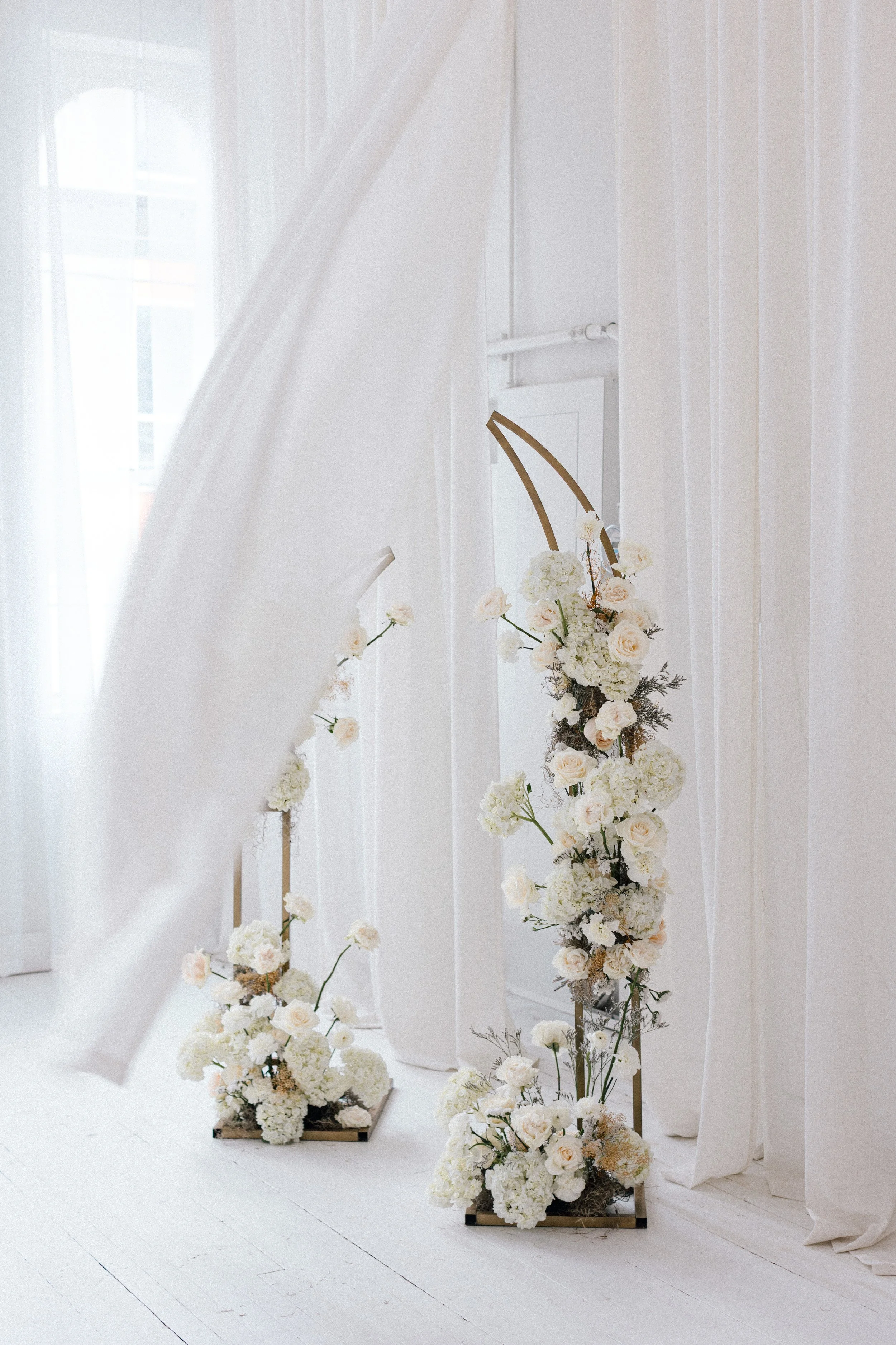 Light fabric blowing through a white floral brand shoot arch