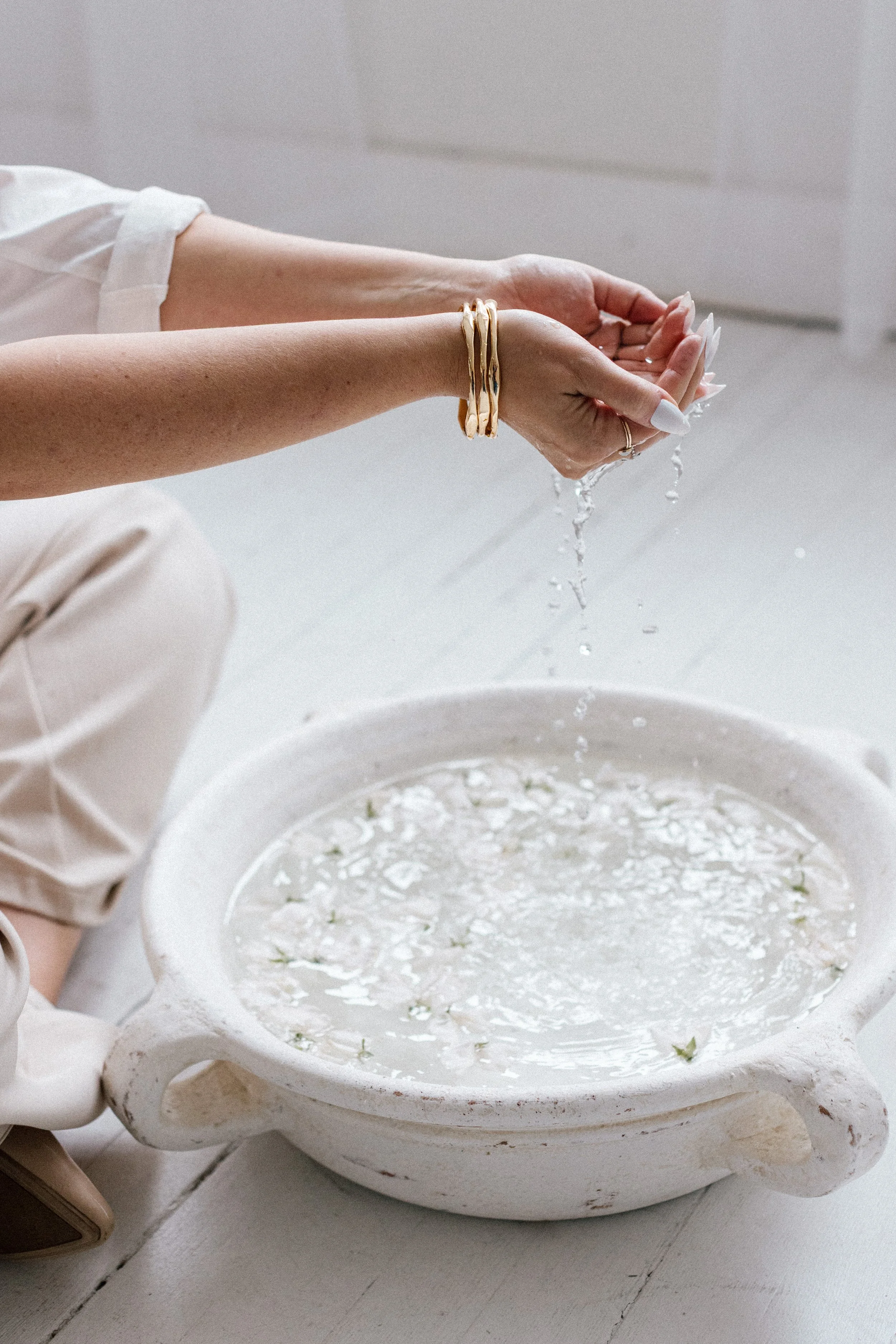 Water dripping through hands into a basin of water with flower petals floating