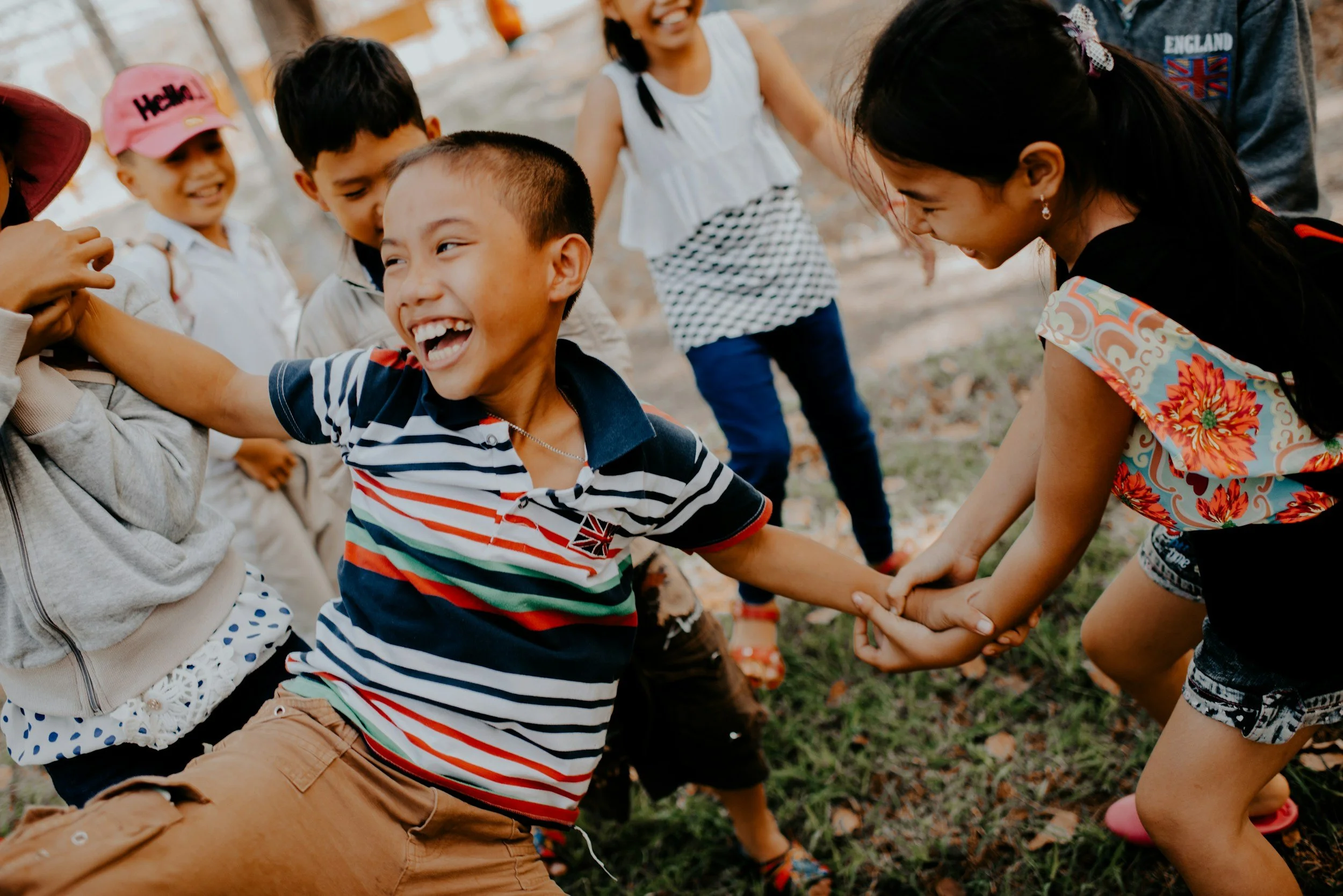 Group of children playing and laughing outdoors, holding hands in a circle.