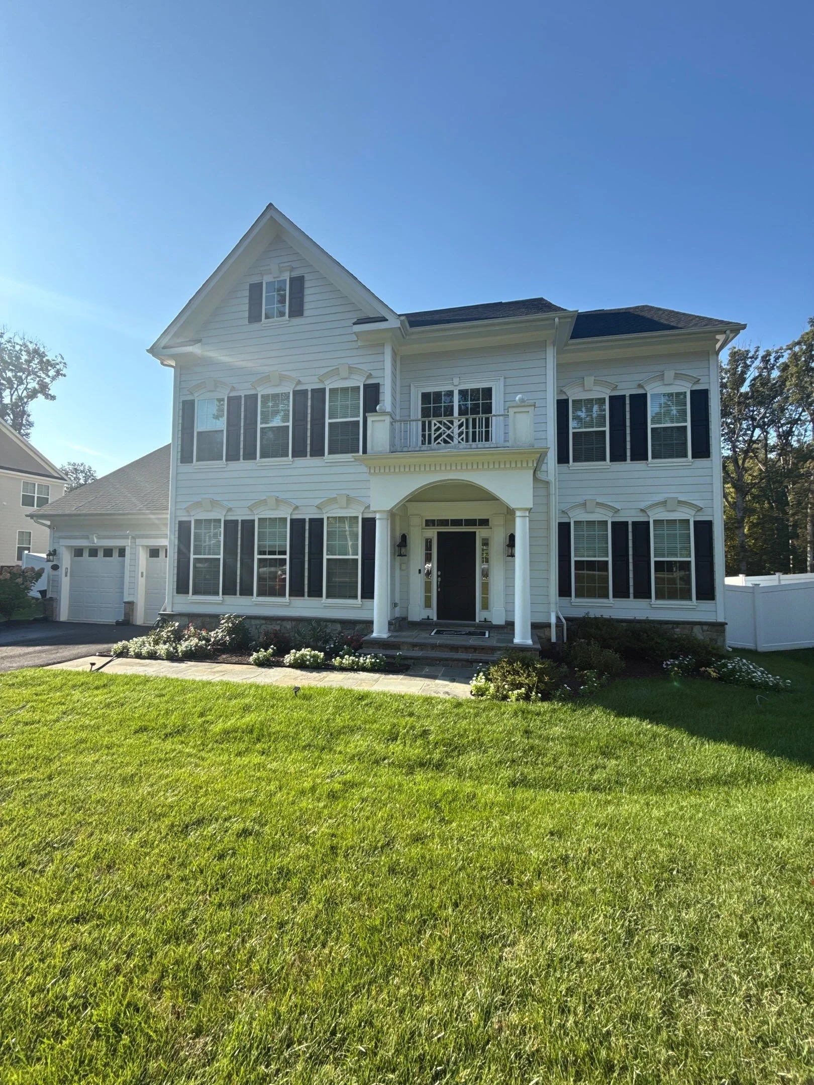 White multi-story house with black shutters, front porch, and a manicured lawn with flowers.