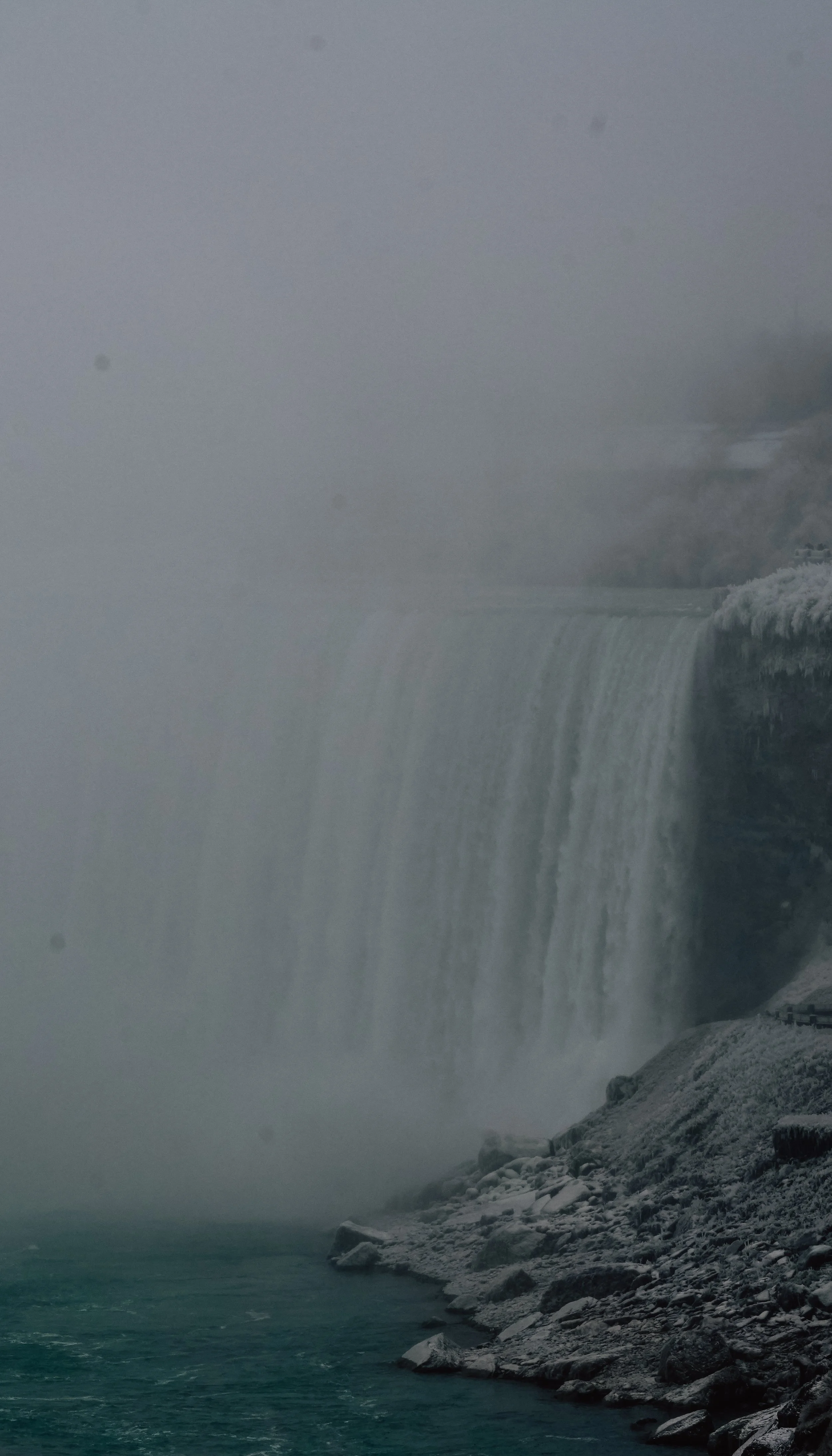 A foggy view of Niagara Falls with water cascading down and rocks at the base.