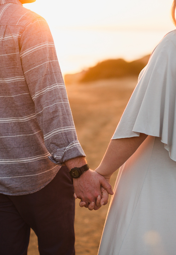 A couple holding hands outdoors during sunset.