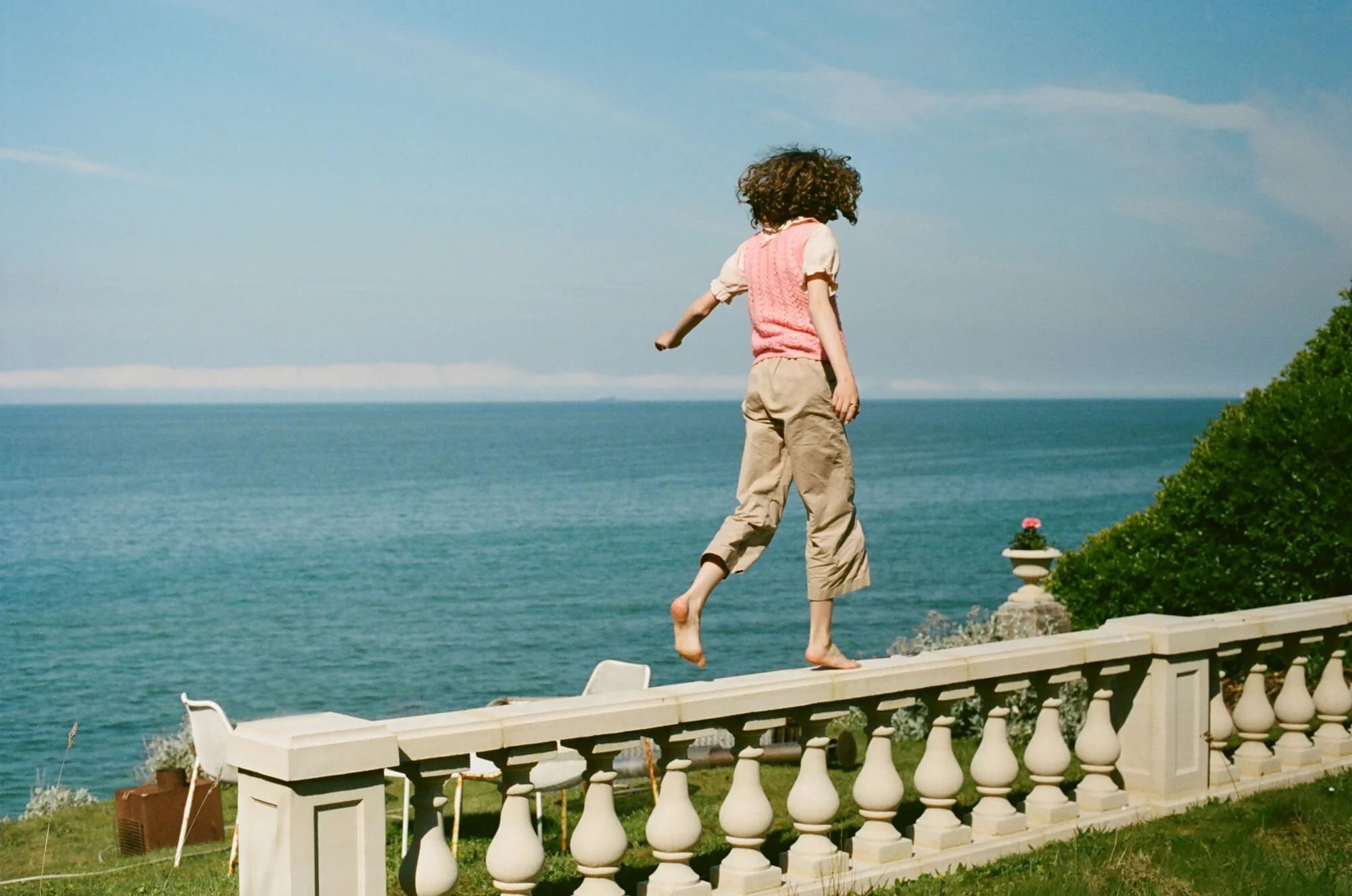 Bunty running along the stone balustrade at Sea Tower, set against the blue sea at the end of the cliff-top garden - a serene coastal scene capturing the location’s charm and open horizon