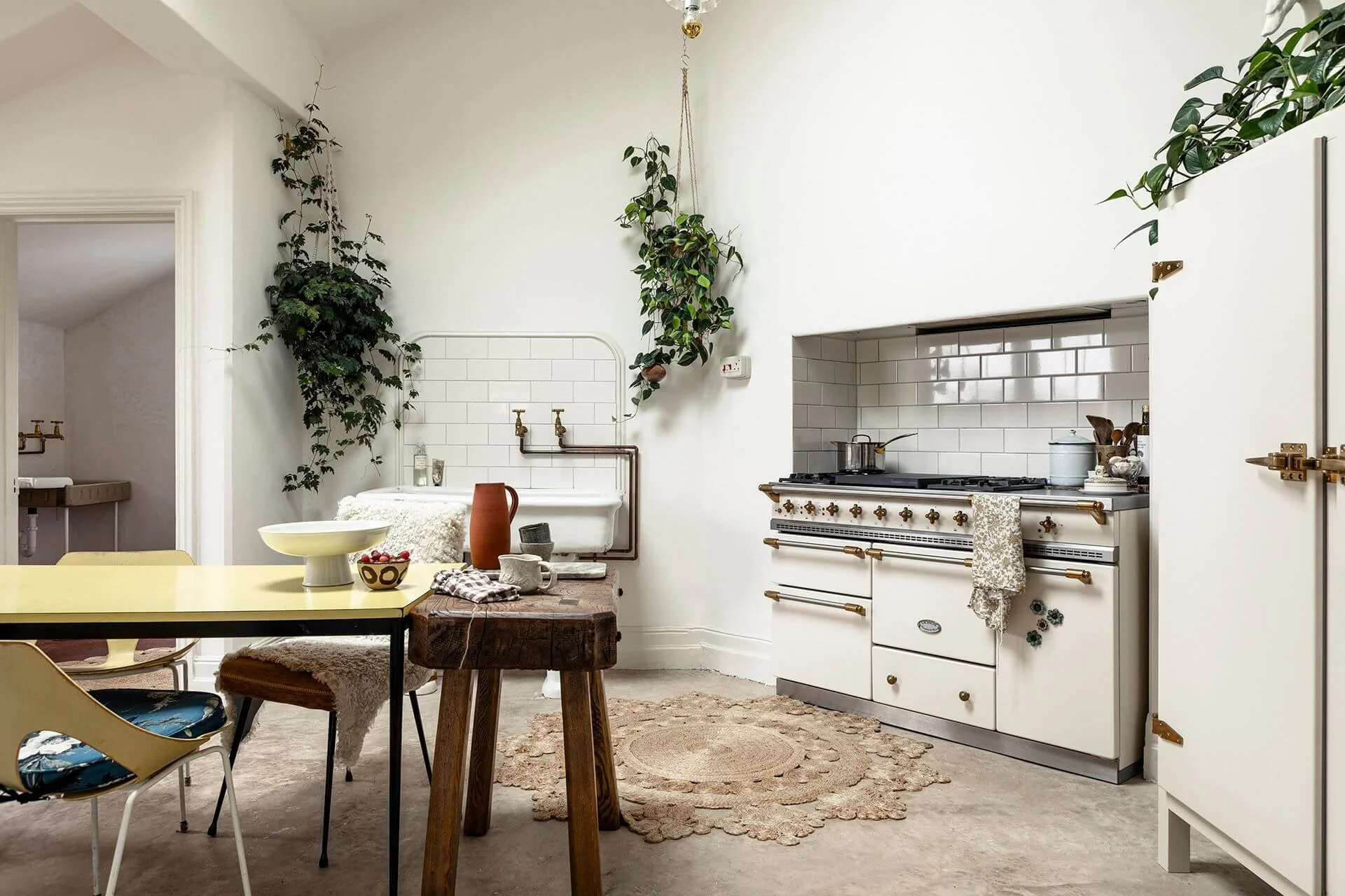 The Sea Tower kitchen with a central table, vintage butcher's block, hanging plants, jute rugs, a Victorian ceramic sink and a Lacanche range cooker.