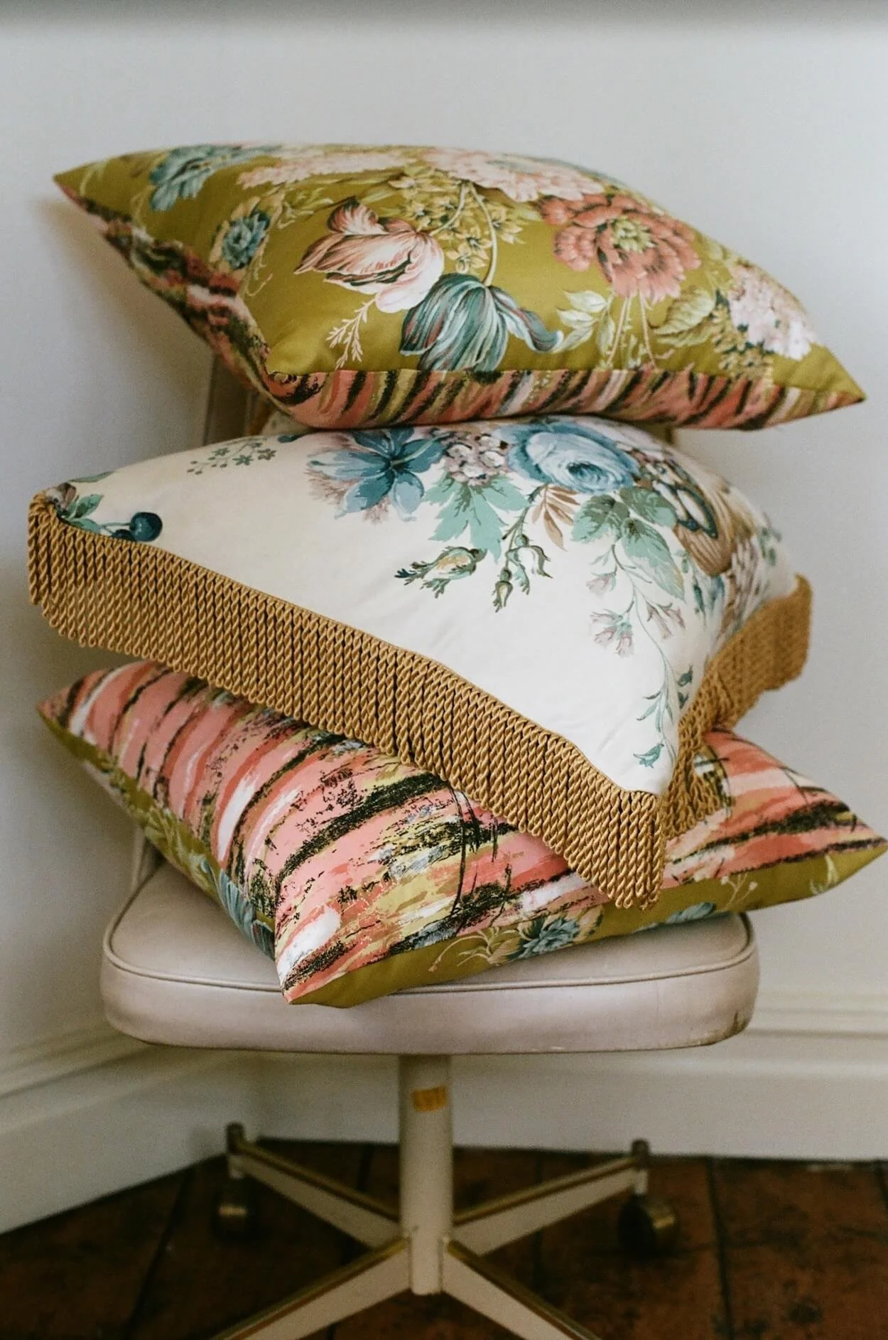 Three vintage floral cushions from the Caravan shop stacked on a vintage chair at Sea Tower.