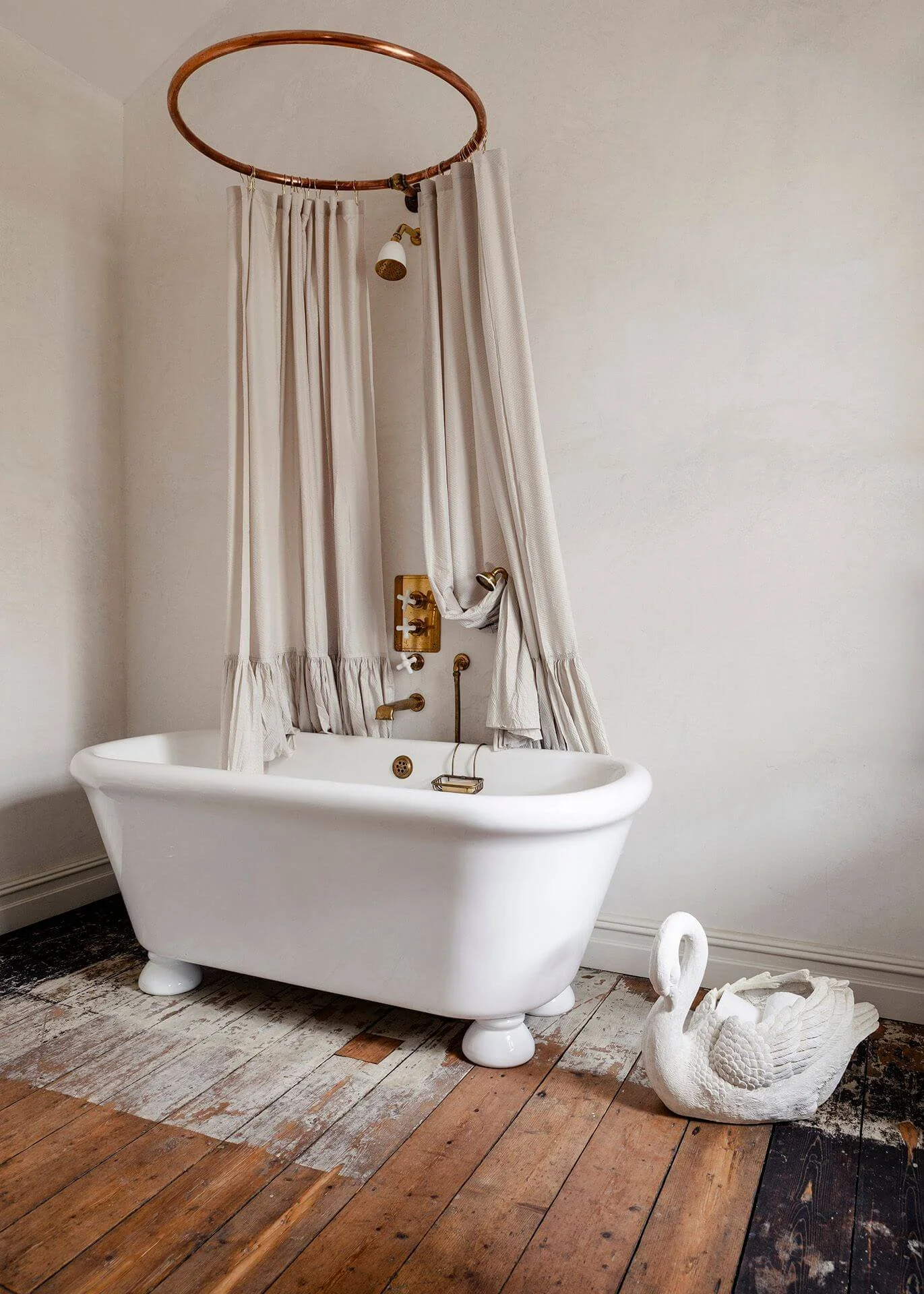 The Sea Tower bathroom with a freestanding bath, brass shower, ruffled shower curtains on a copper rail and a swan vessel beside the bath.
