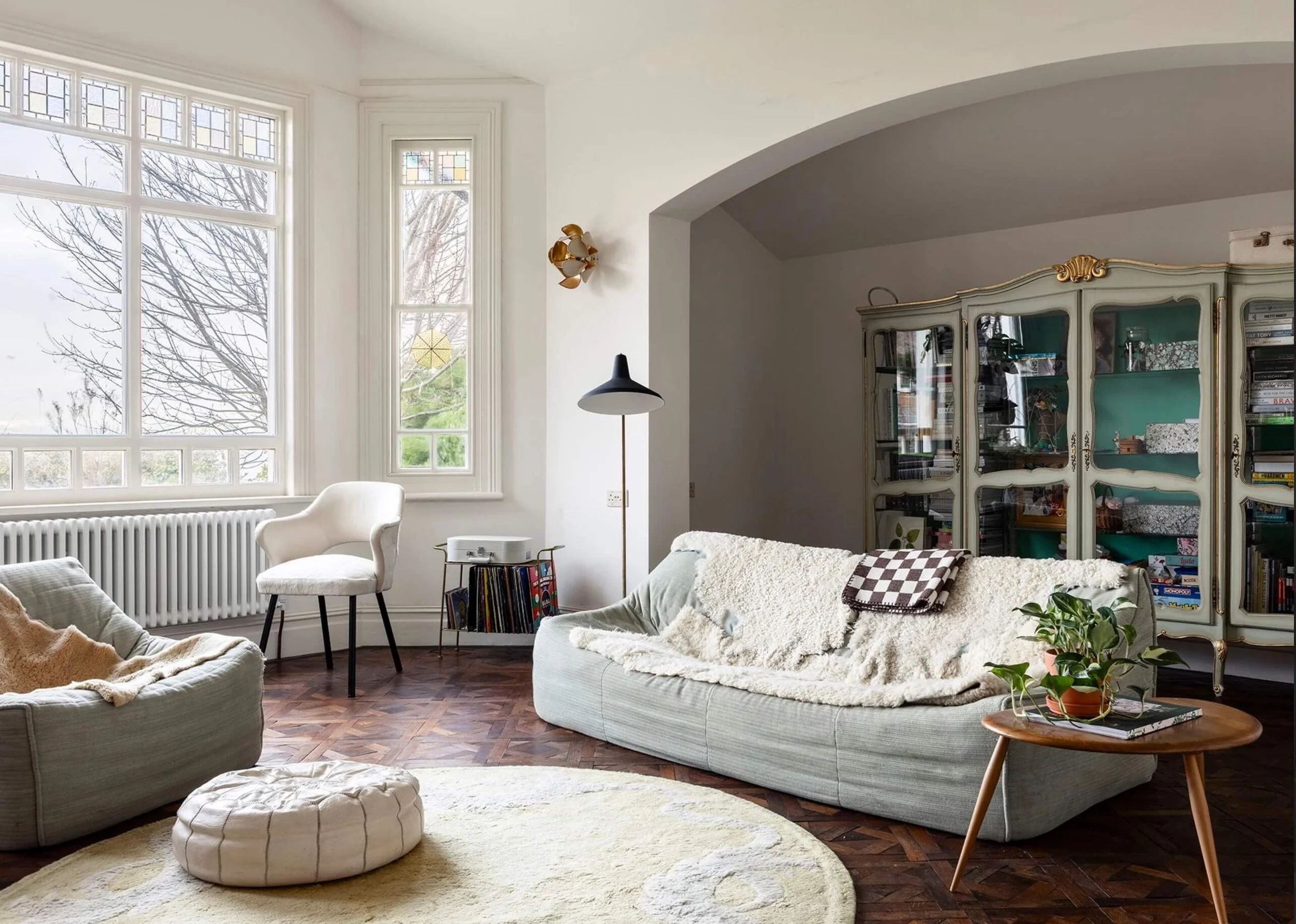 The Sea Tower living room with Ligne Roset seating, a vintage side table, rug, pouffe and a cabinet filled with books and games.