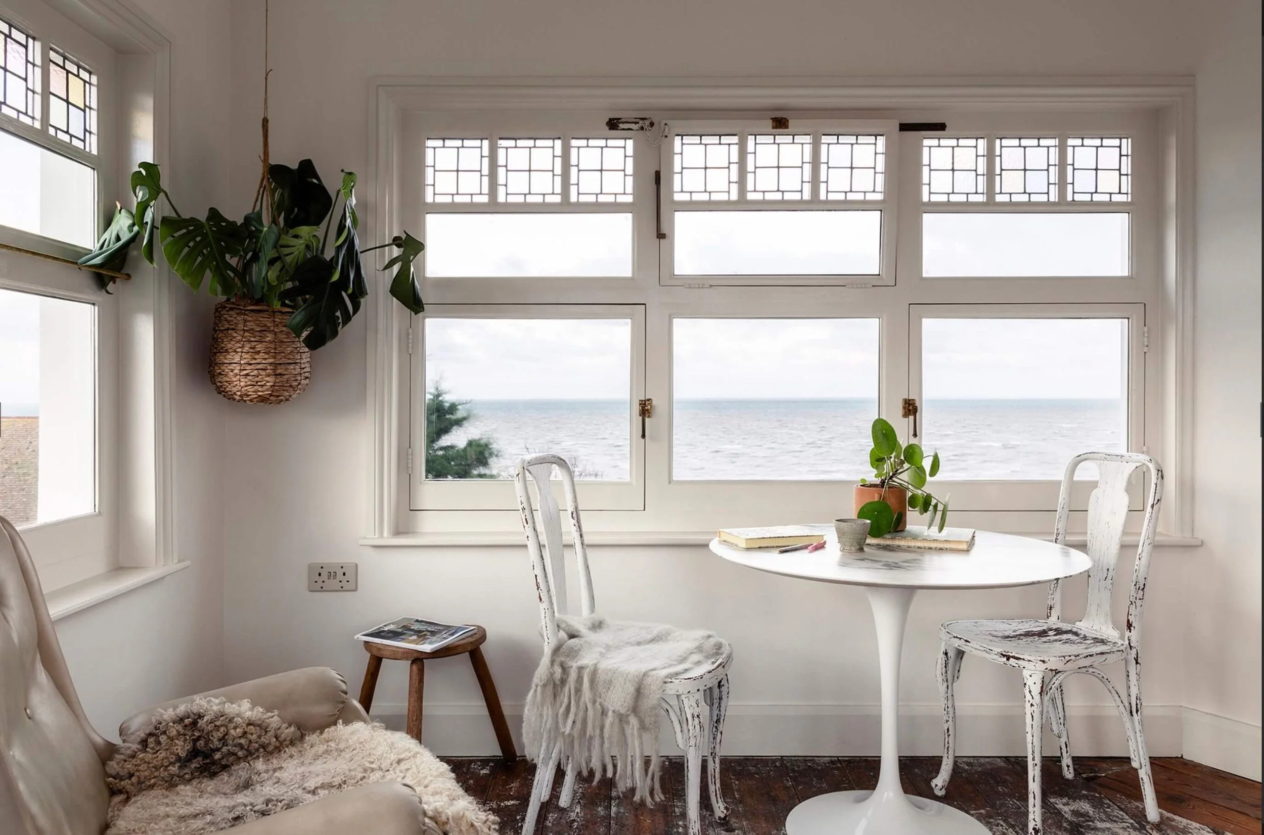 The top tower room at Sea Tower with panoramic sea views, a Knoll tulip table and vintage chairs, hanging plant, and a vintage swivel arm chair.