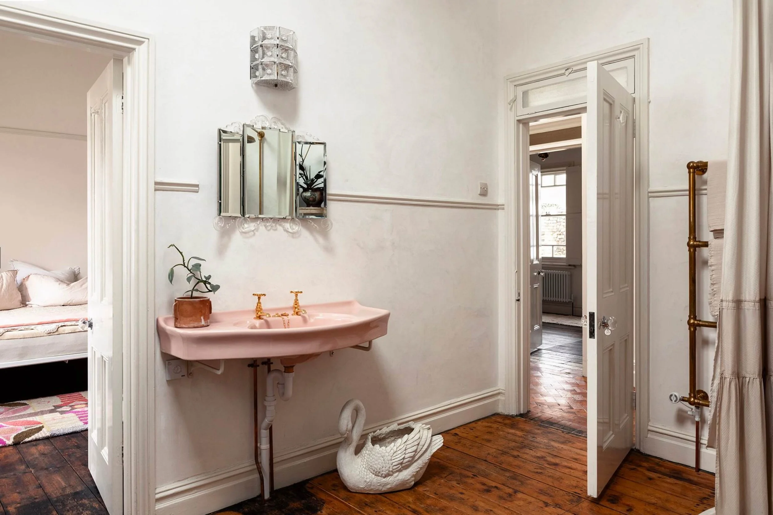 The Sea Tower shower room with a pink washbasin, gold taps, and a decorative swan on the original wooden floor, holding toiletries.