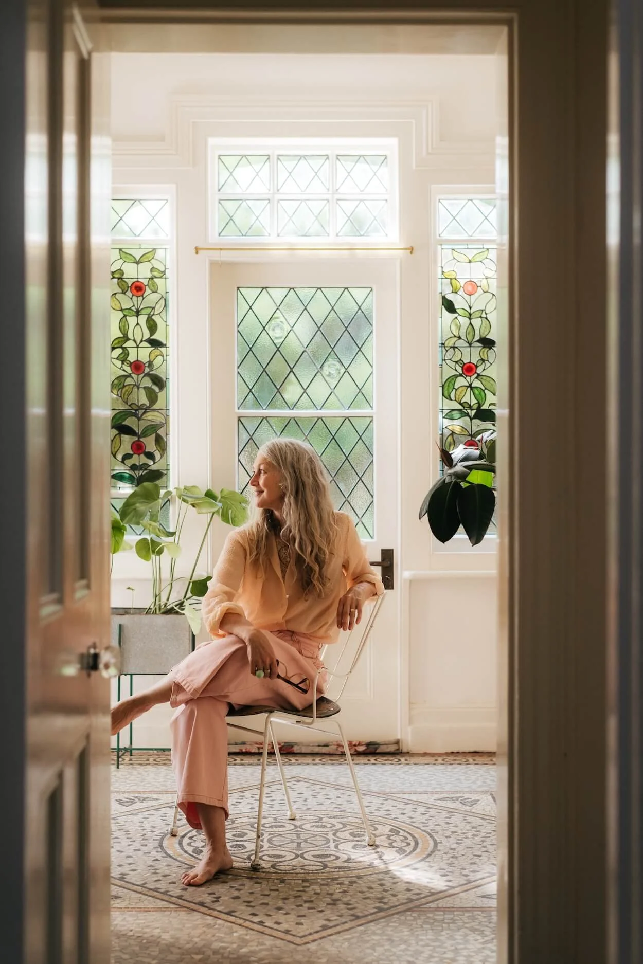 Emily Chalmers sitting on a vintage chair in the entrance hall of Sea Tower, with the original Victorian mosaic tiled floor.