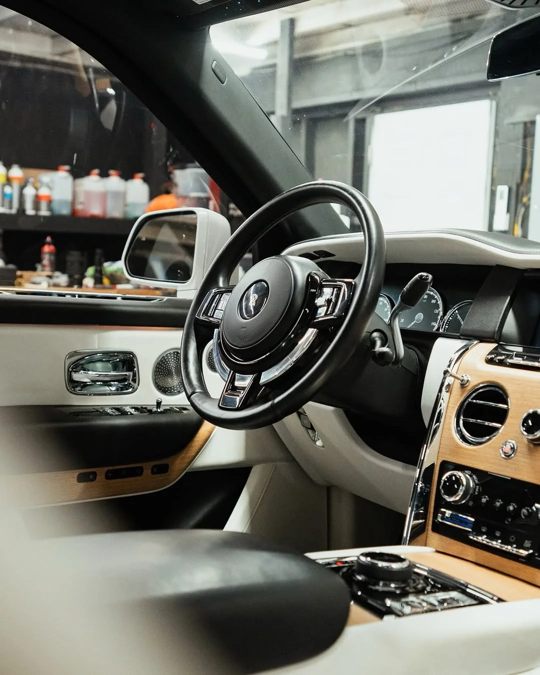 Interior of a luxury car showing a black steering wheel, dashboard with gauges, and a wood-trimmed center console.
